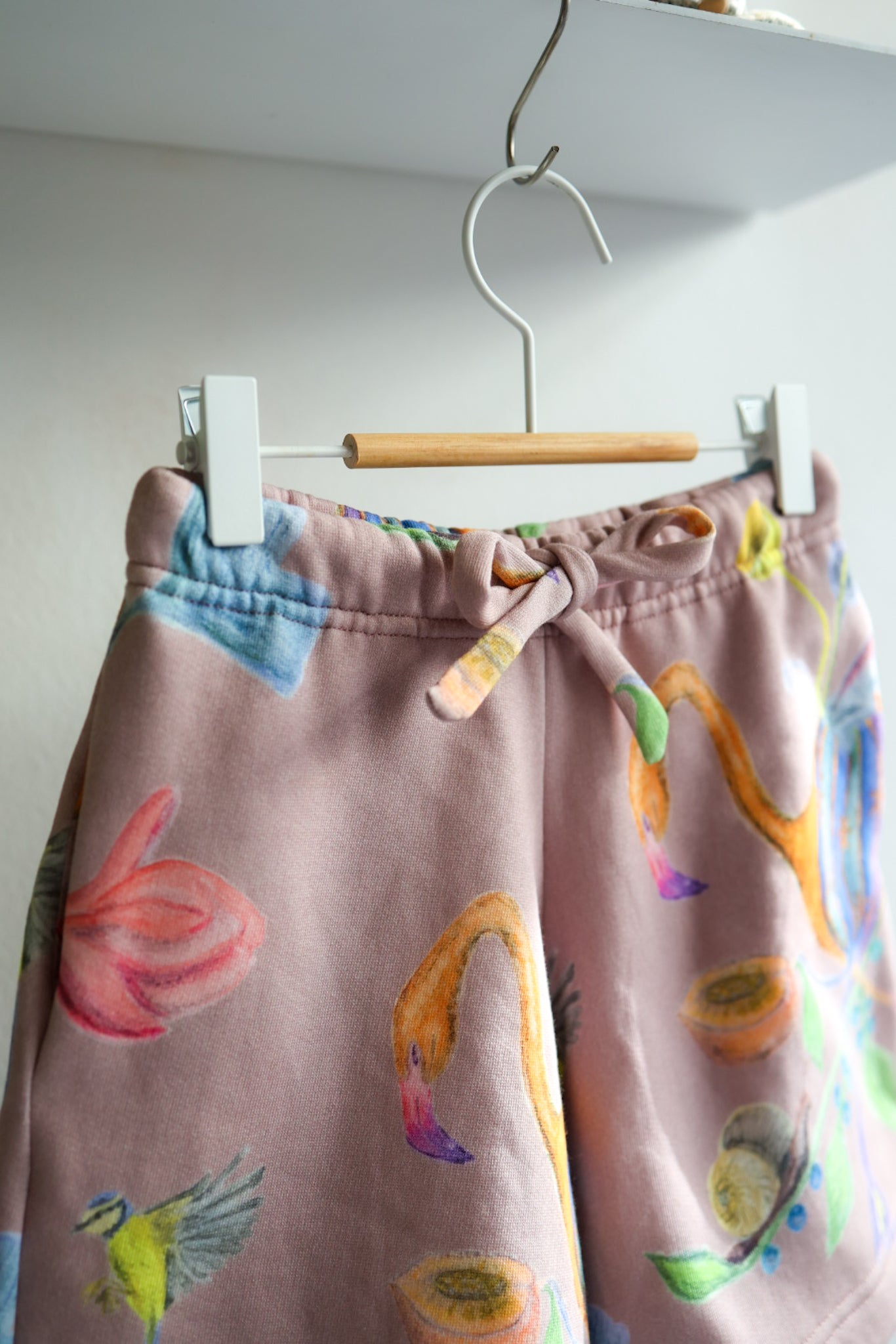 Colorful children's shorts with floral patterns on a hanger against a white wall.