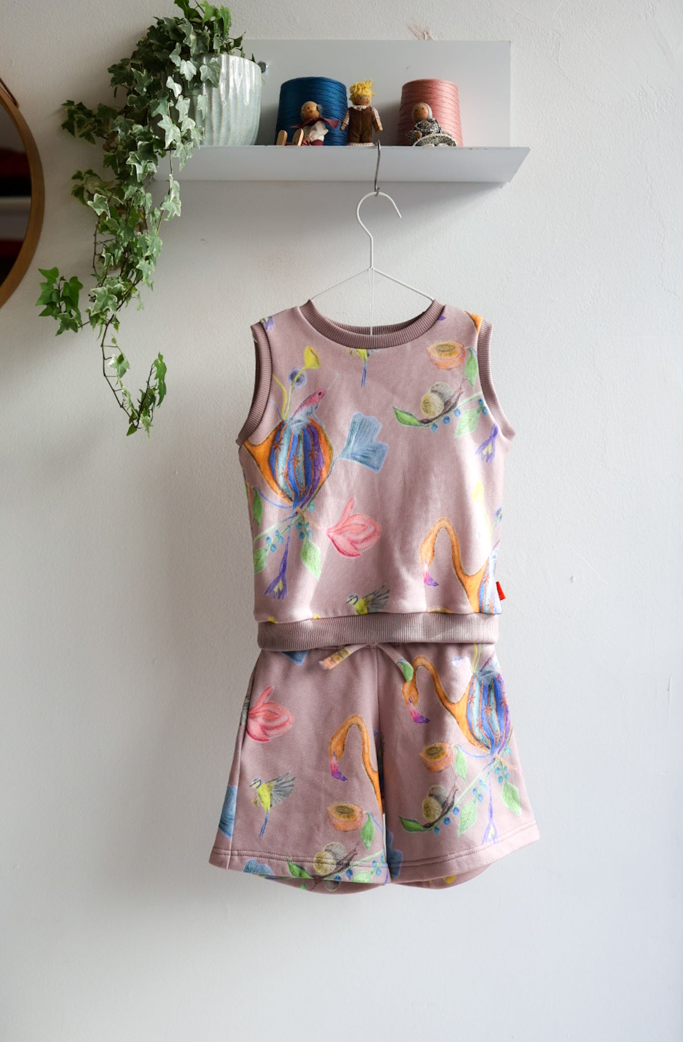 Children's sleeveless top and shorts set with colorful designs on a white wall.