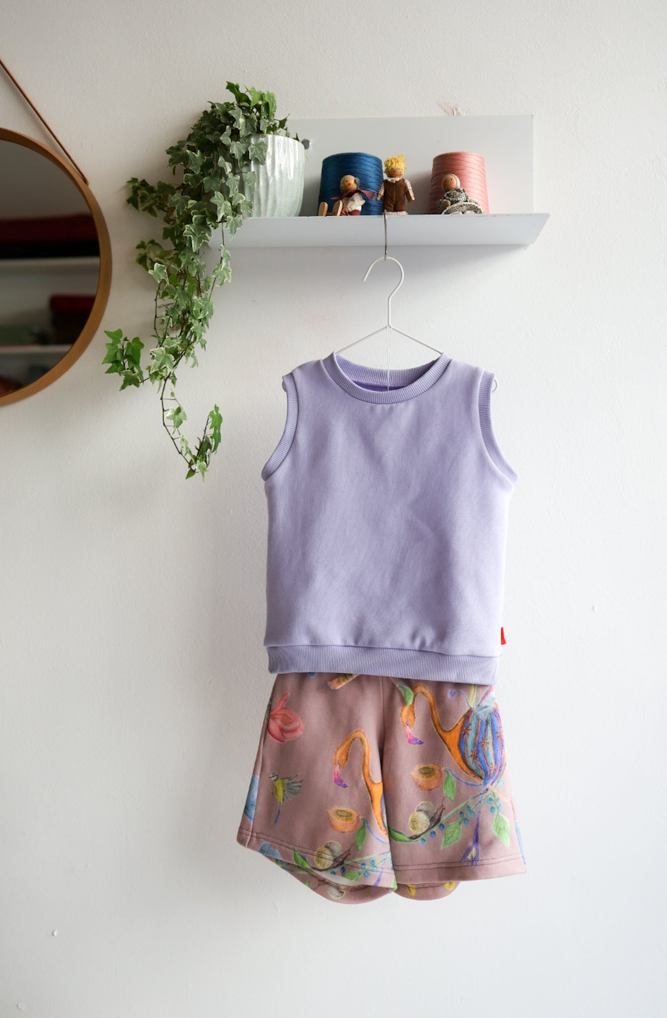 Children's sleeveless top and shorts set on a hanger against a white wall with decorative elements.