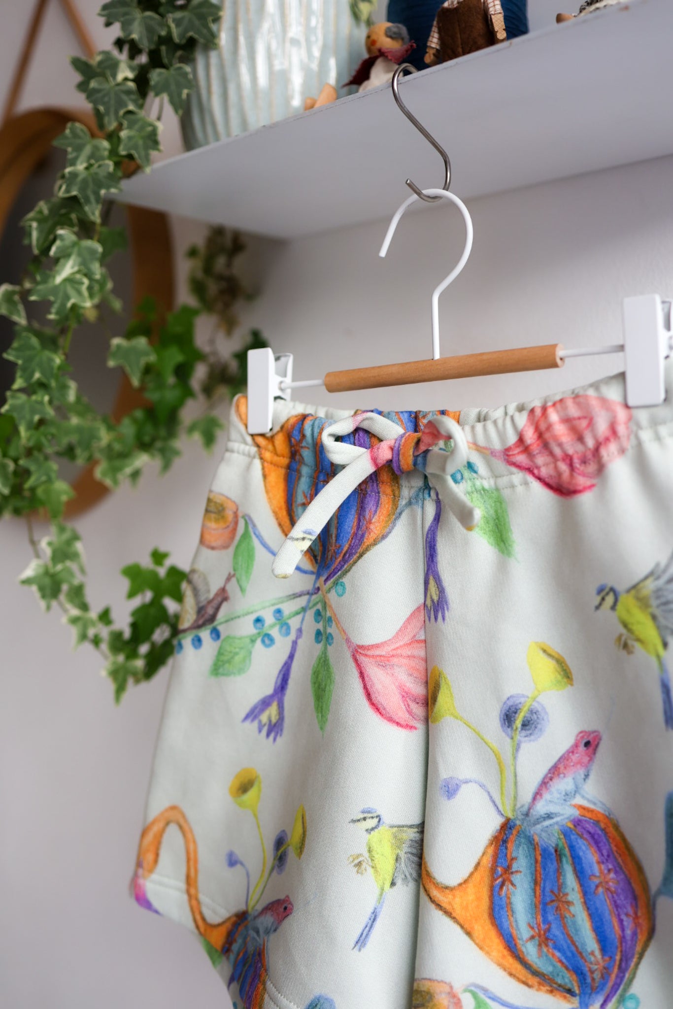 Colorful shorts with floral pattern hanging on a hook against a white wall.