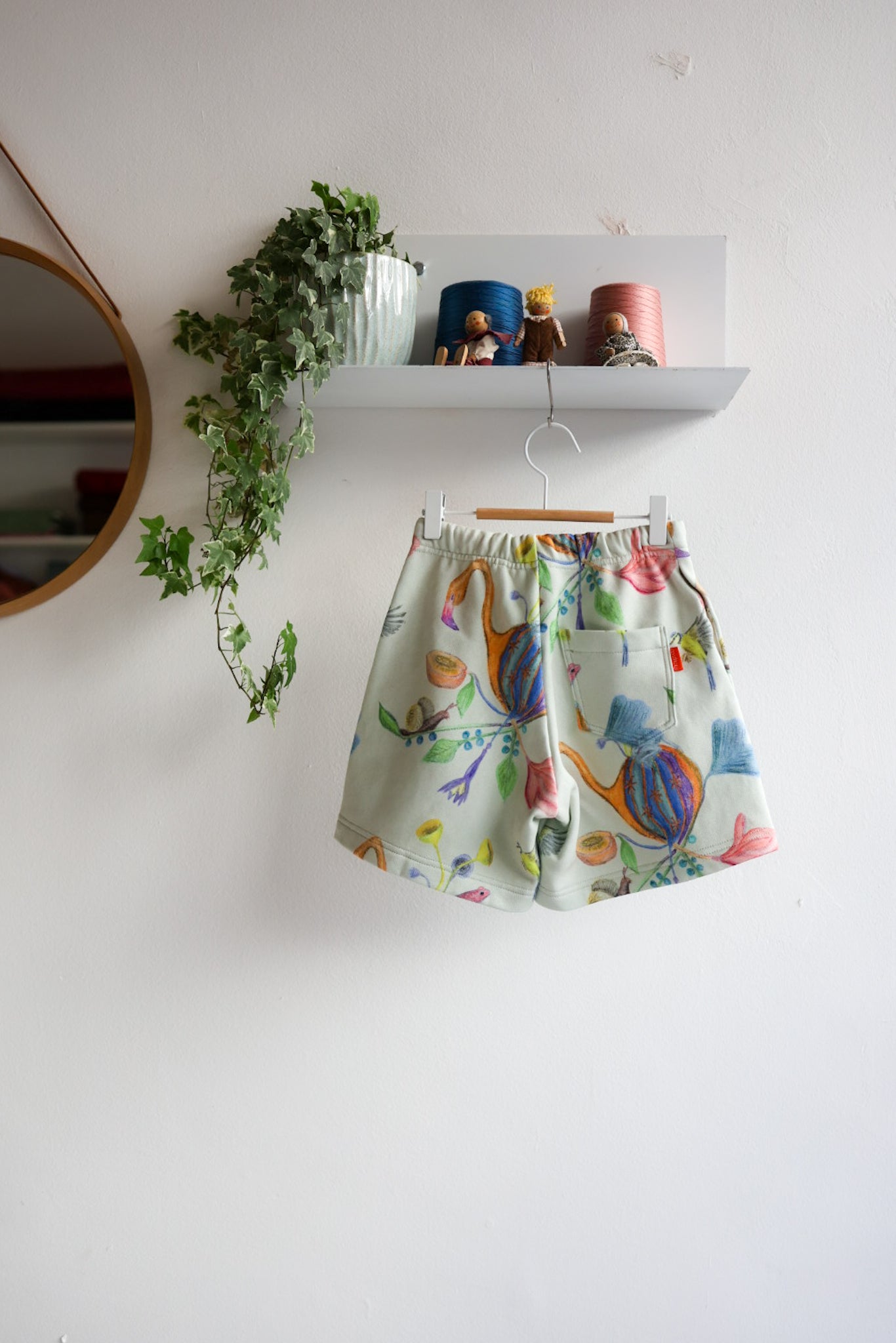 Colorful kids shorts with fruit pattern hanging on a white wall.