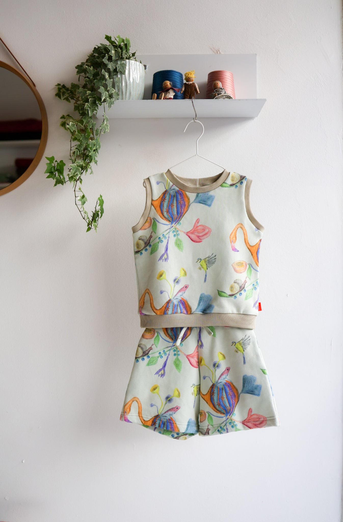 Kids's sleeveless top and shorts set with colorful designs on a white wall.