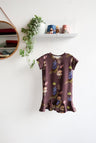 Brown kids dress with nature-themed pattern on a hanger against a white wall.