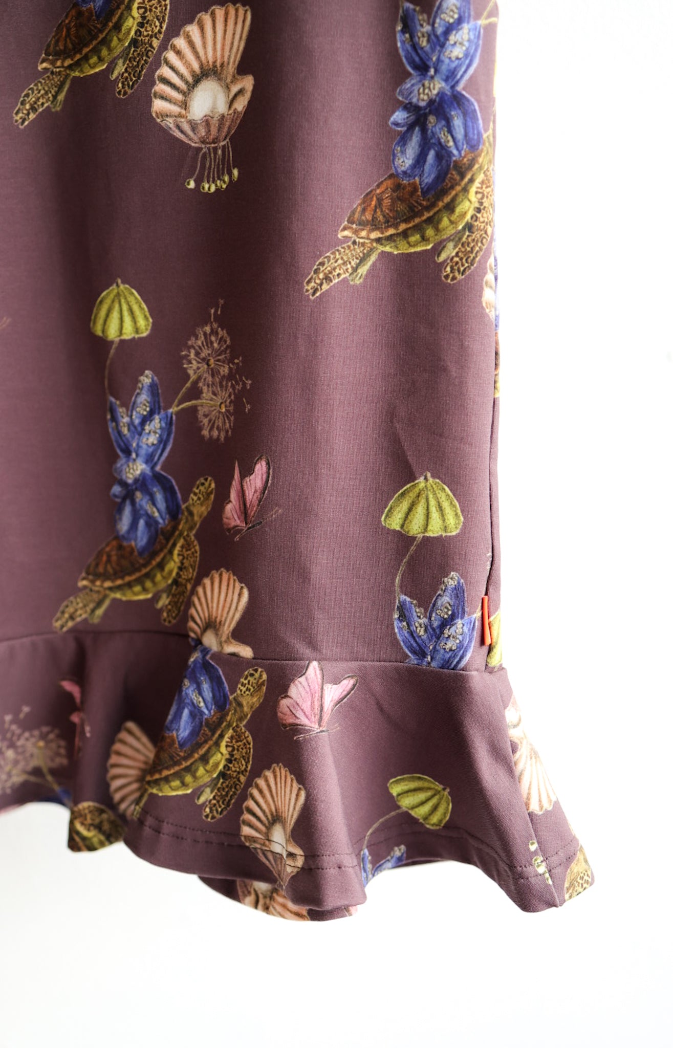 Close-up of a brown kids dress with nature-themed pattern against a white wall.