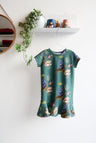 Teal kids dress with nature-themed pattern on a hanger against a white wall.