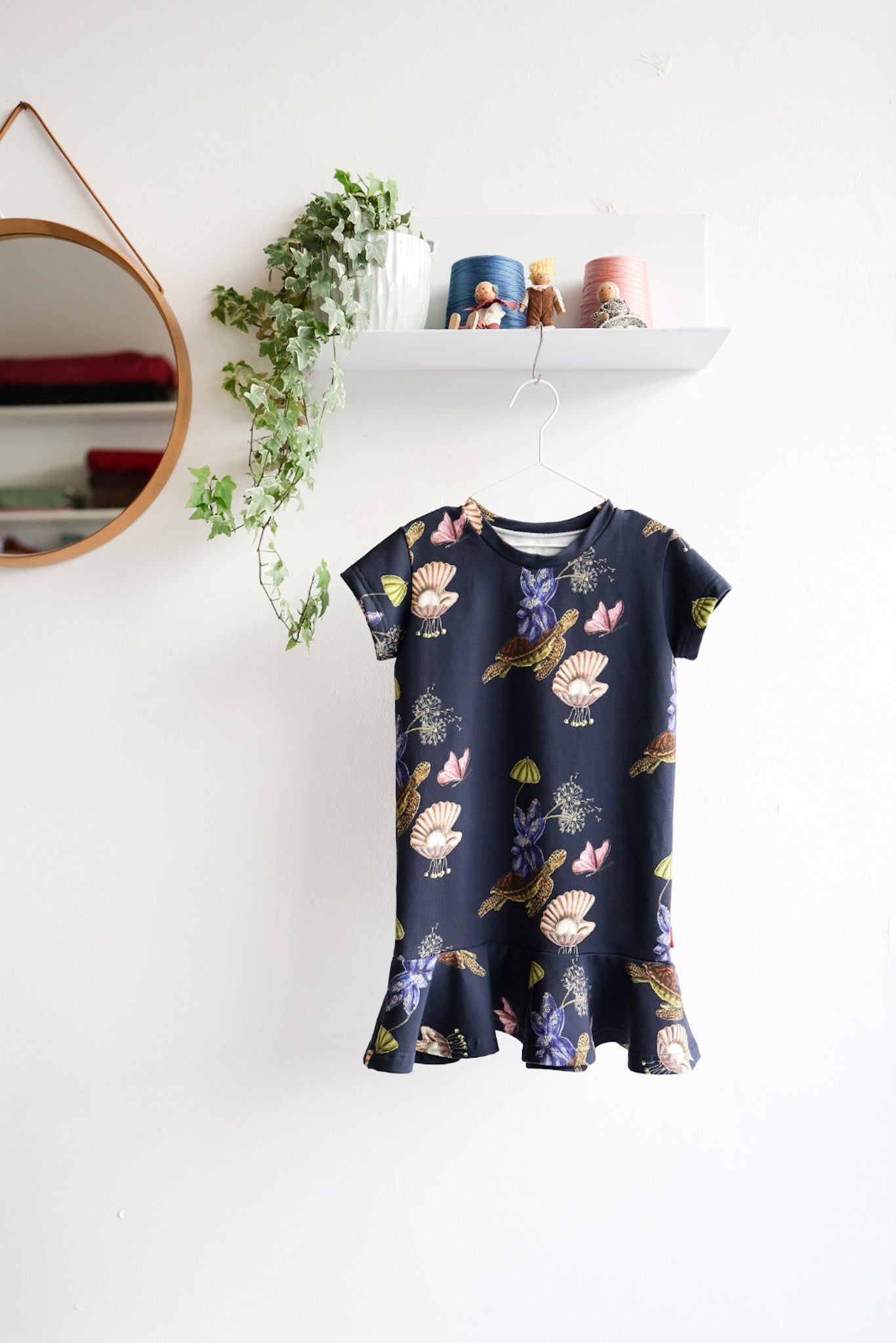 Navy blue kids dress with nature-themed pattern on a hanger against a white wall.