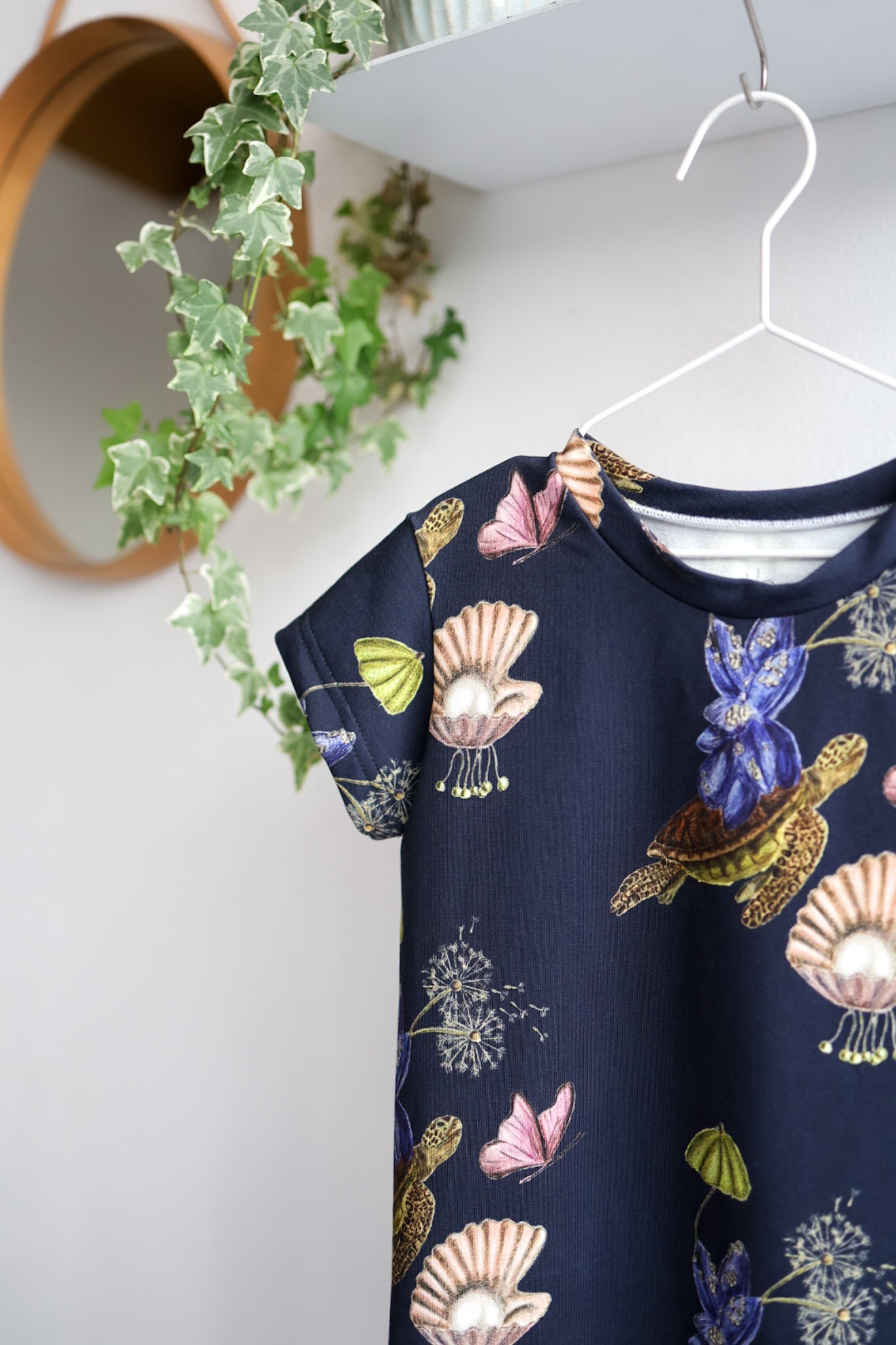 Navy blue kids dress with nature-themed pattern on a hanger against a white wall.