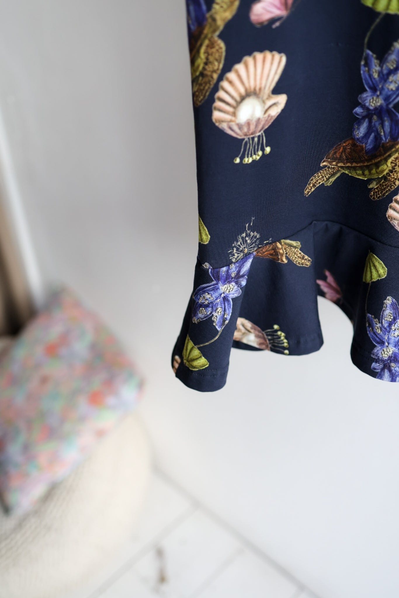 Navy blue kids dress with nature-themed pattern on a hanger against a white wall.