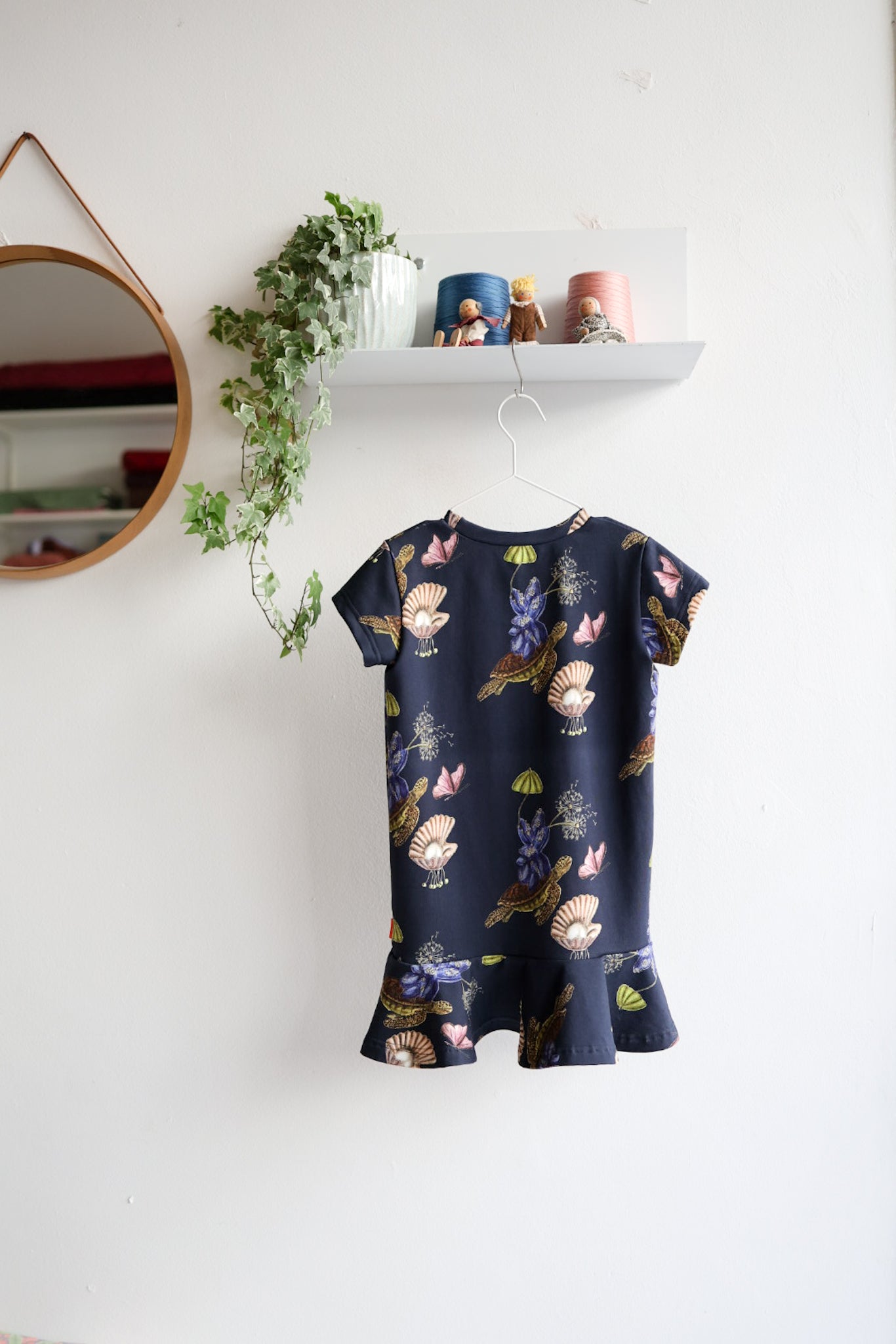 Navy blue kids dress with nature-themed pattern on a hanger against a white wall.