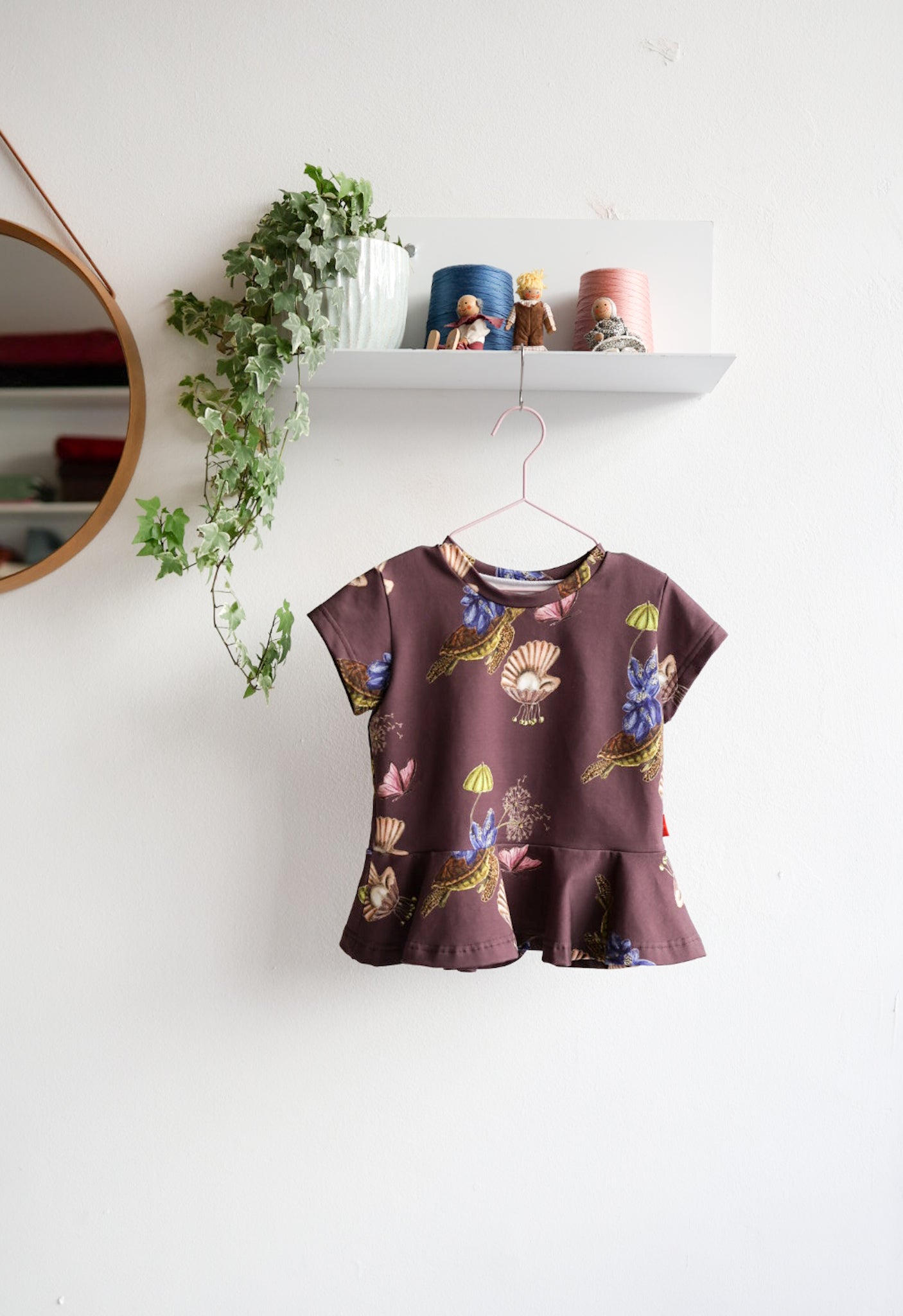 Kids nature-themed print top hanging on a white wall with decorative items.