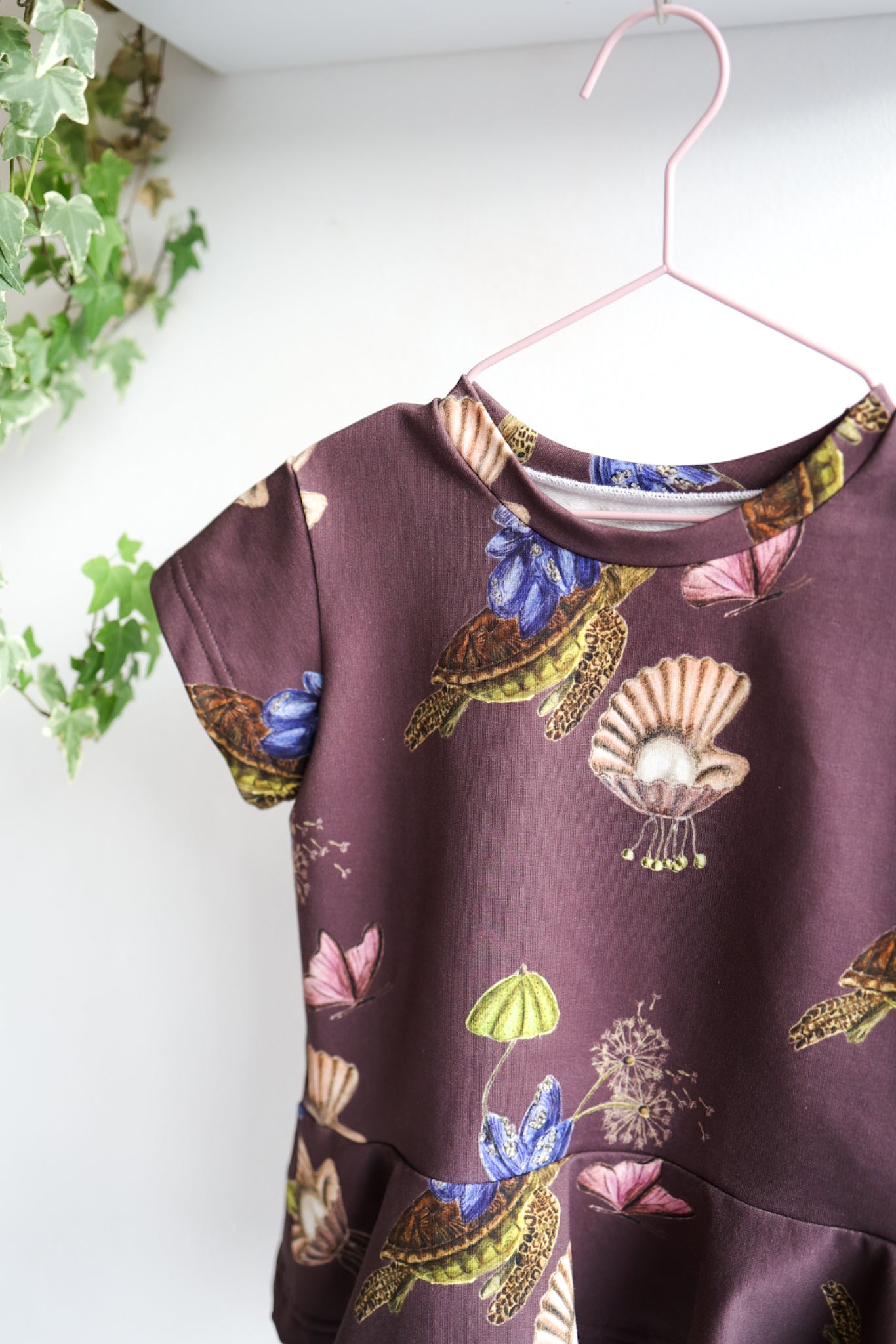Kids nature-themed print top hanging on a white wall with decorative items.