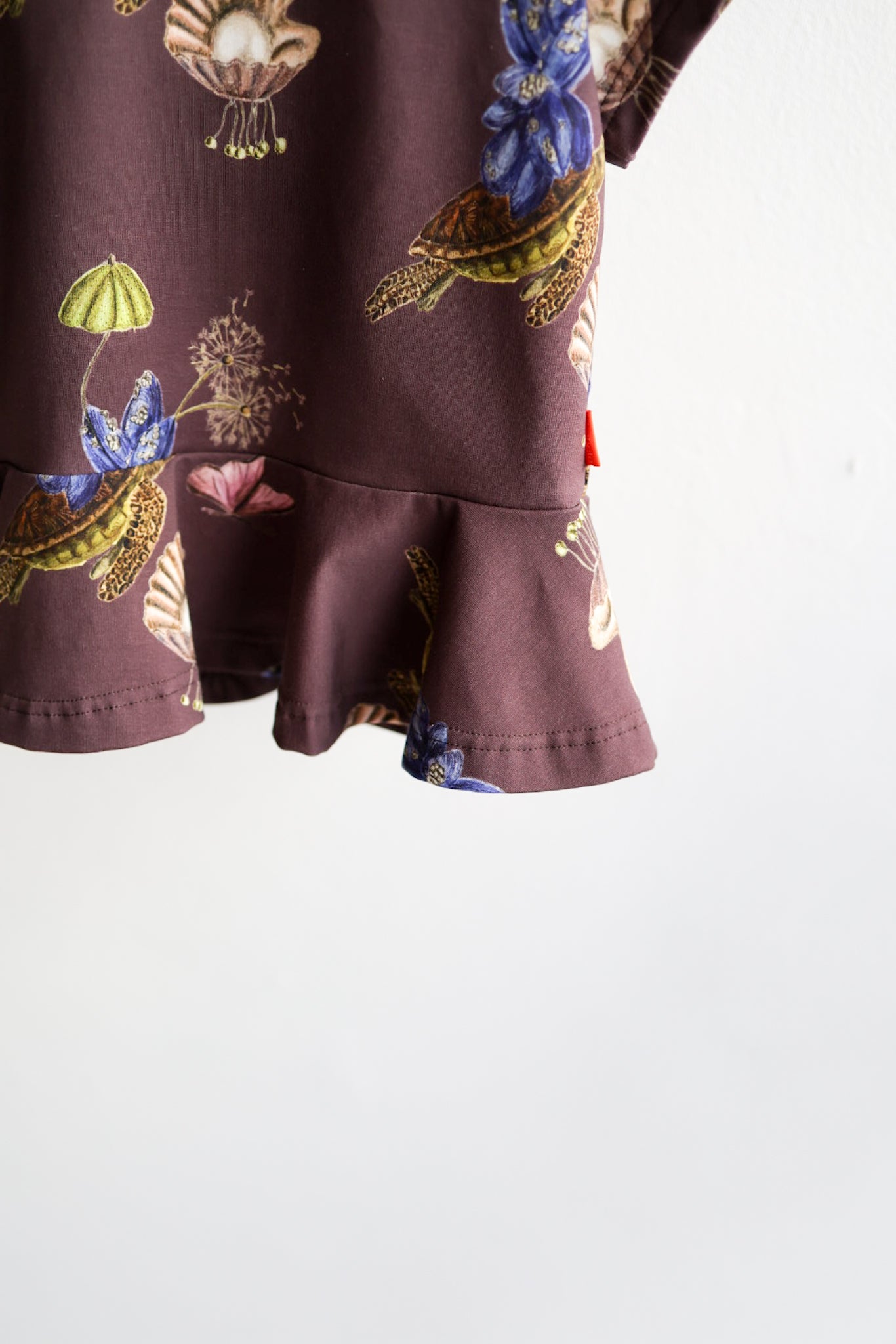 Close-up of a kids nature-themed print top standing against a white wall.