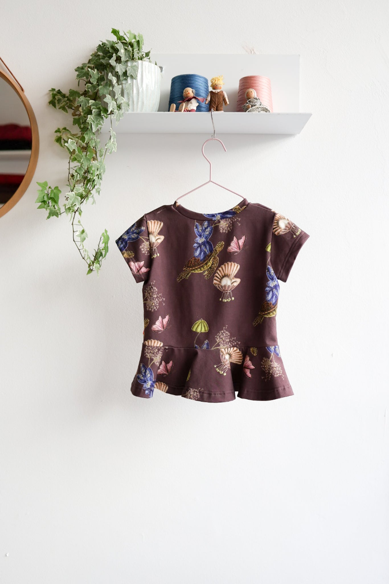 Kids nature-themed print top hanging on a white wall with decorative items.
