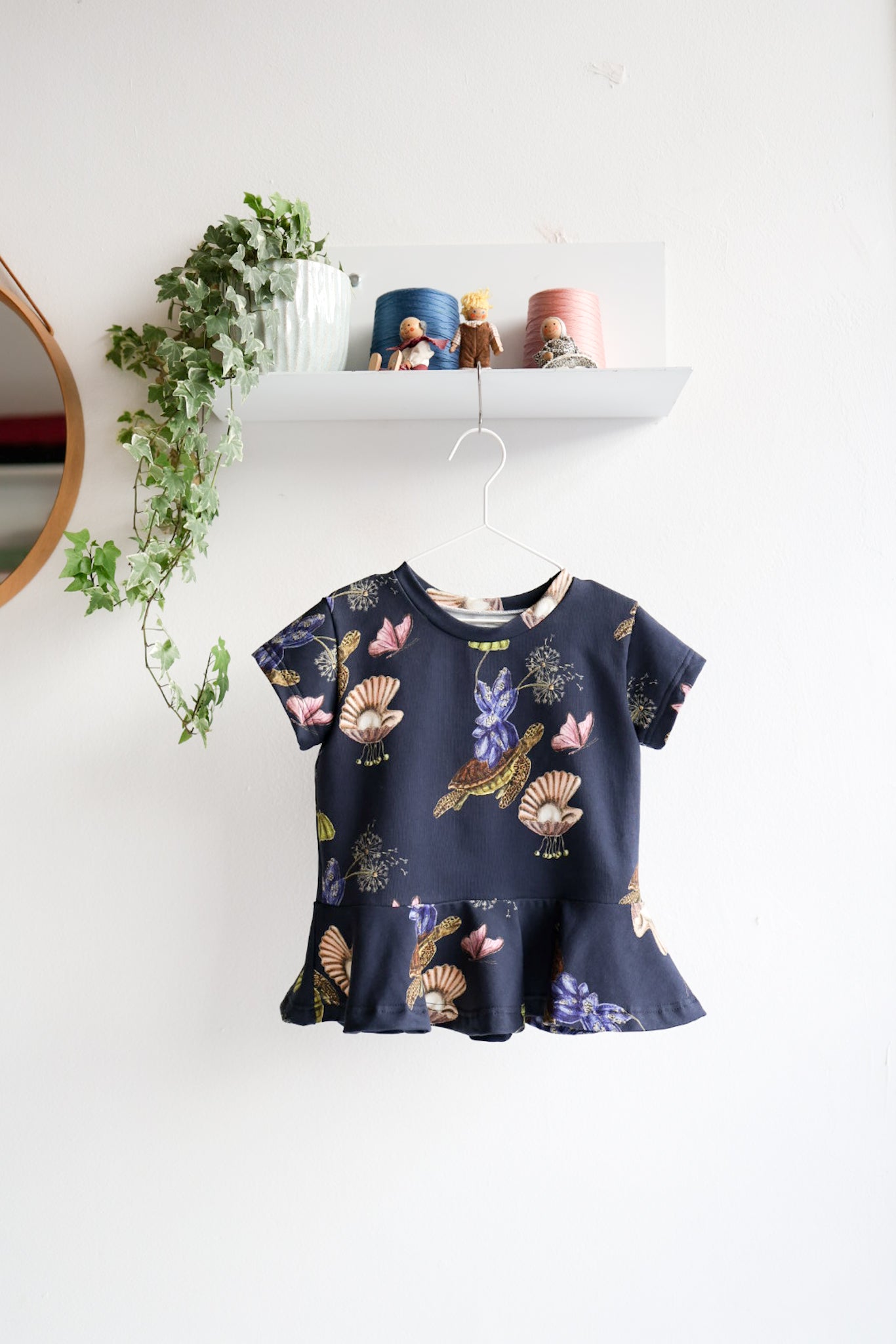 Navy blue kids top with colorful shell pattern hanging on a white wall.