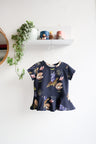 Navy blue kids top with colorful shell pattern hanging on a white wall.