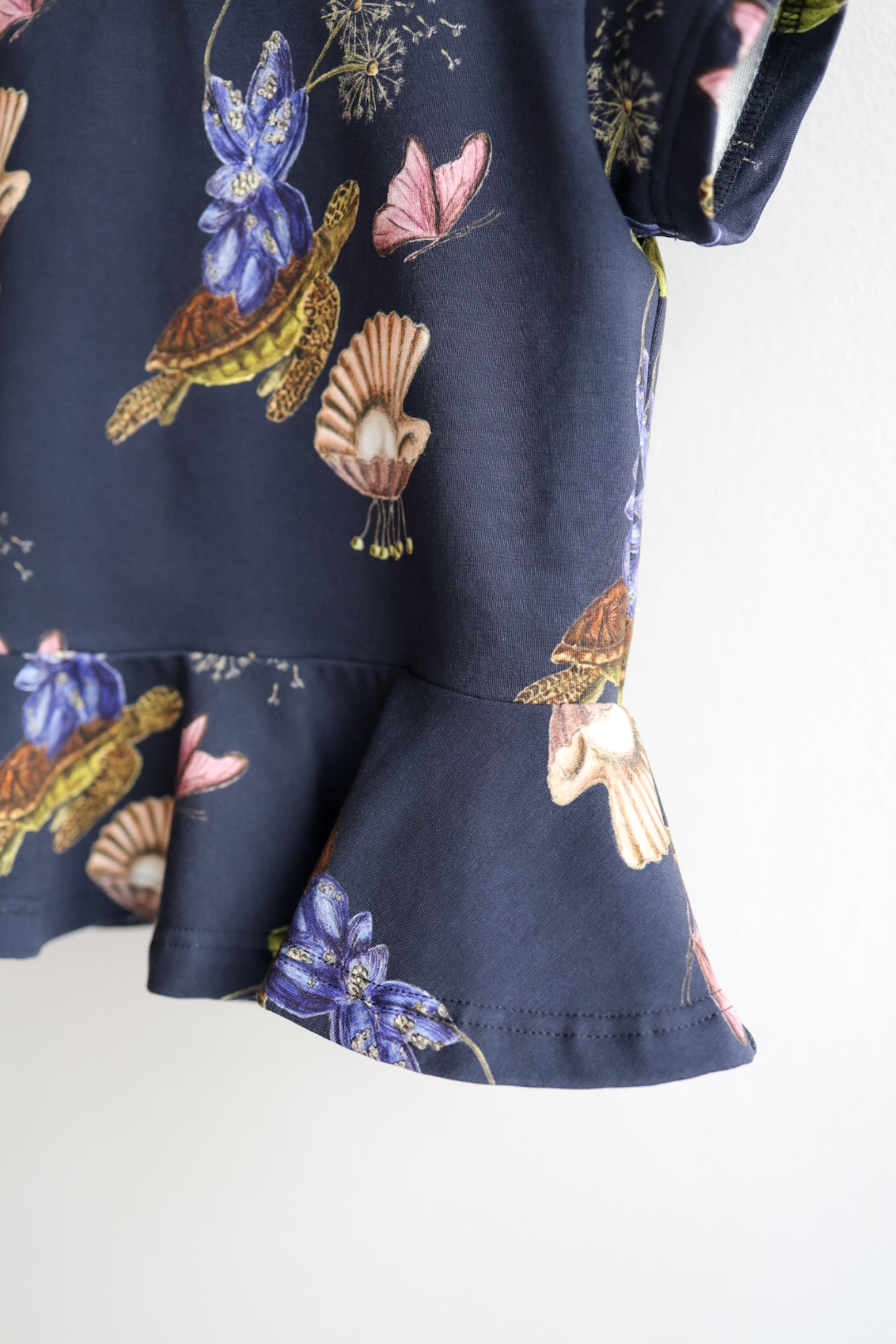 Close-up of a navy blue kids top with colorful shell pattern hanging on a white wall.