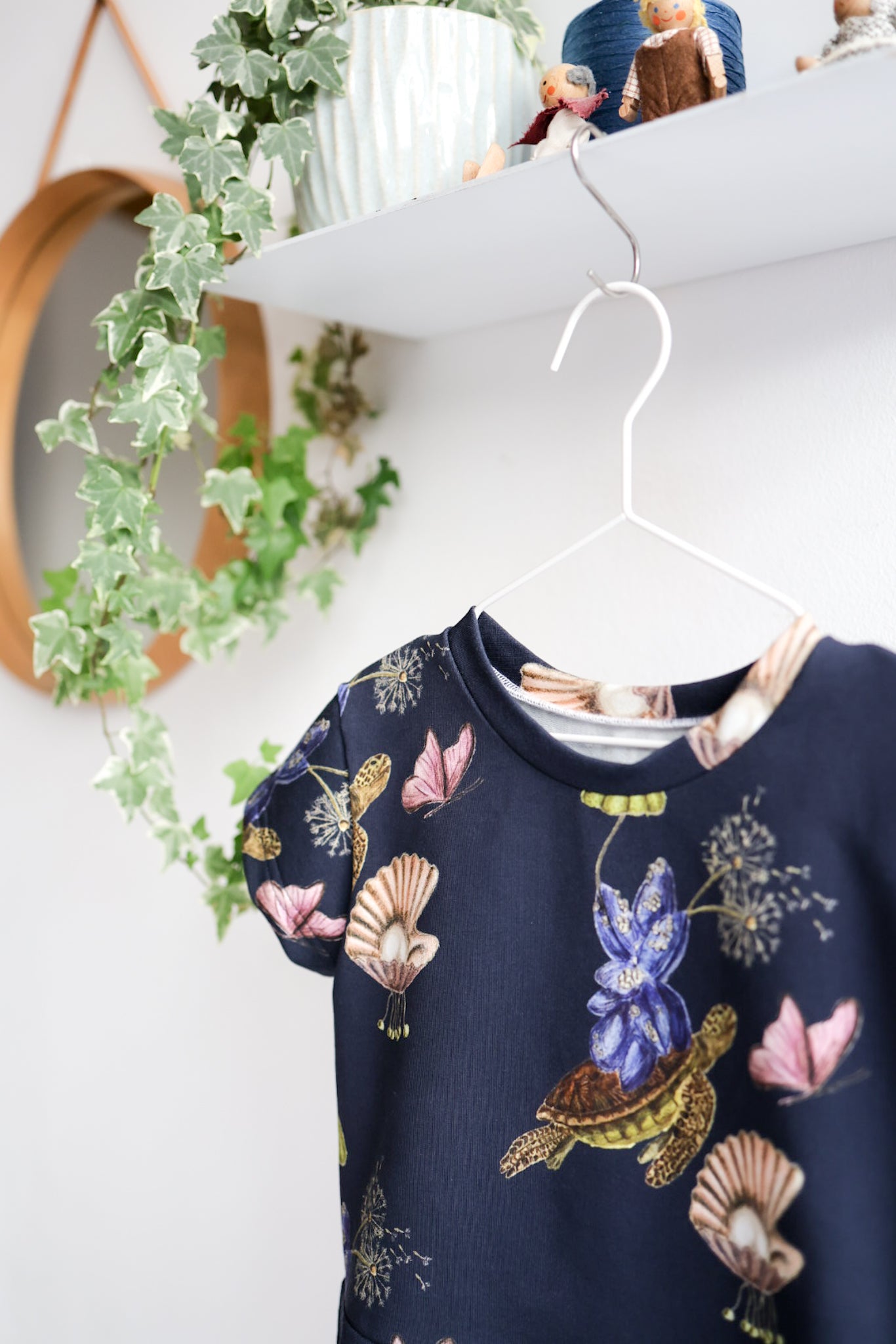 Navy blue kids top with colorful shell pattern hanging on a white wall.