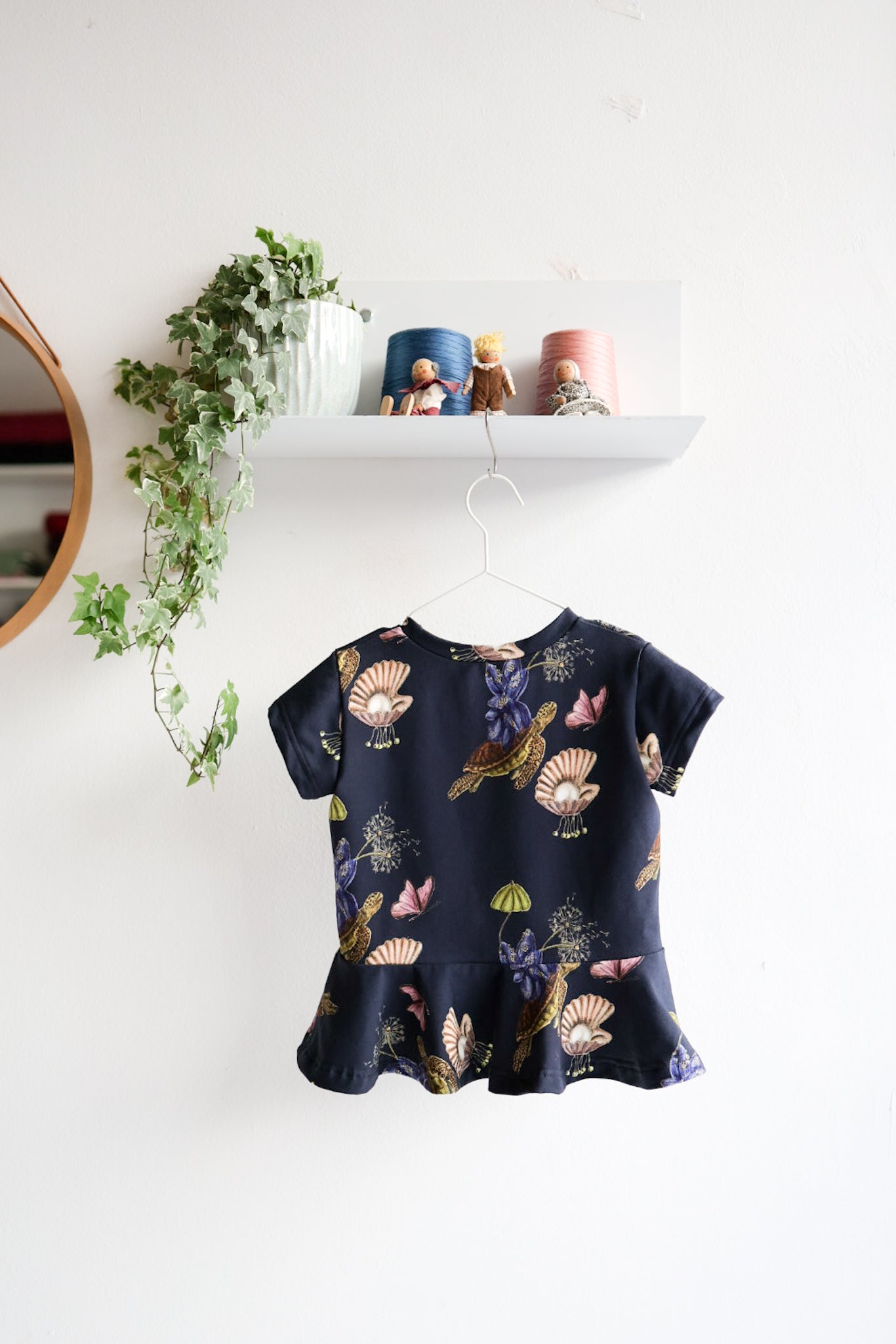 Navy blue kids top with colorful shell pattern hanging on a white wall.