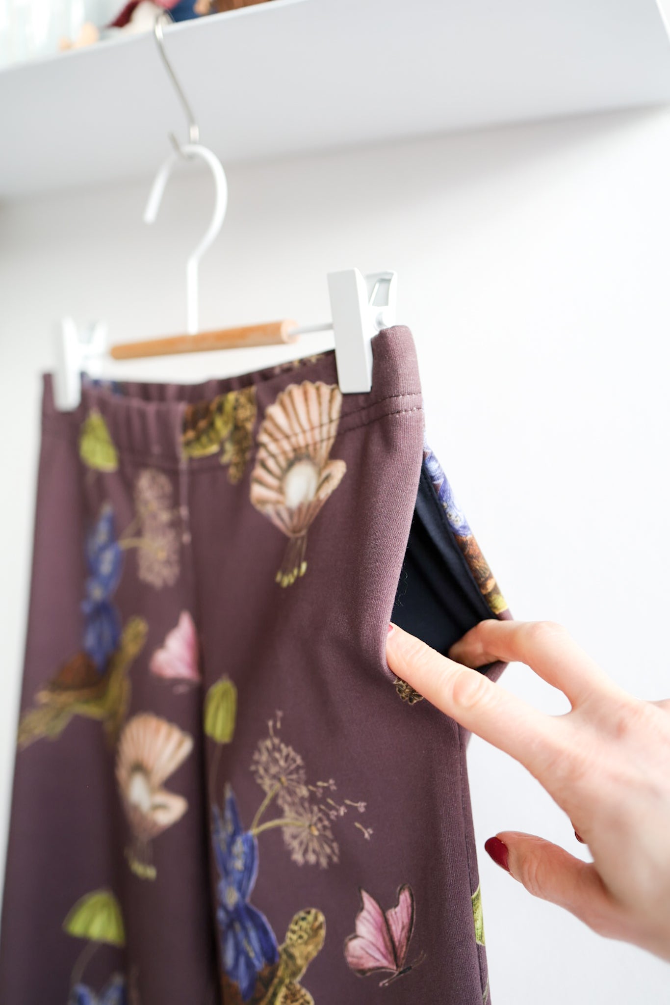 Brown nature-patterned kids pants on a hanger with a hand reaching towards them.