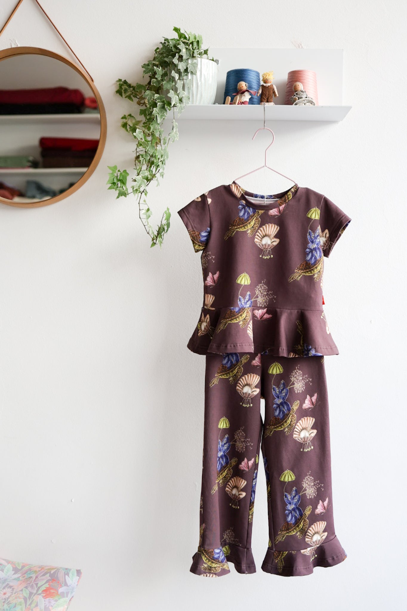 Nature-patterned kids pants and top hanging against a white wall with decorative items.