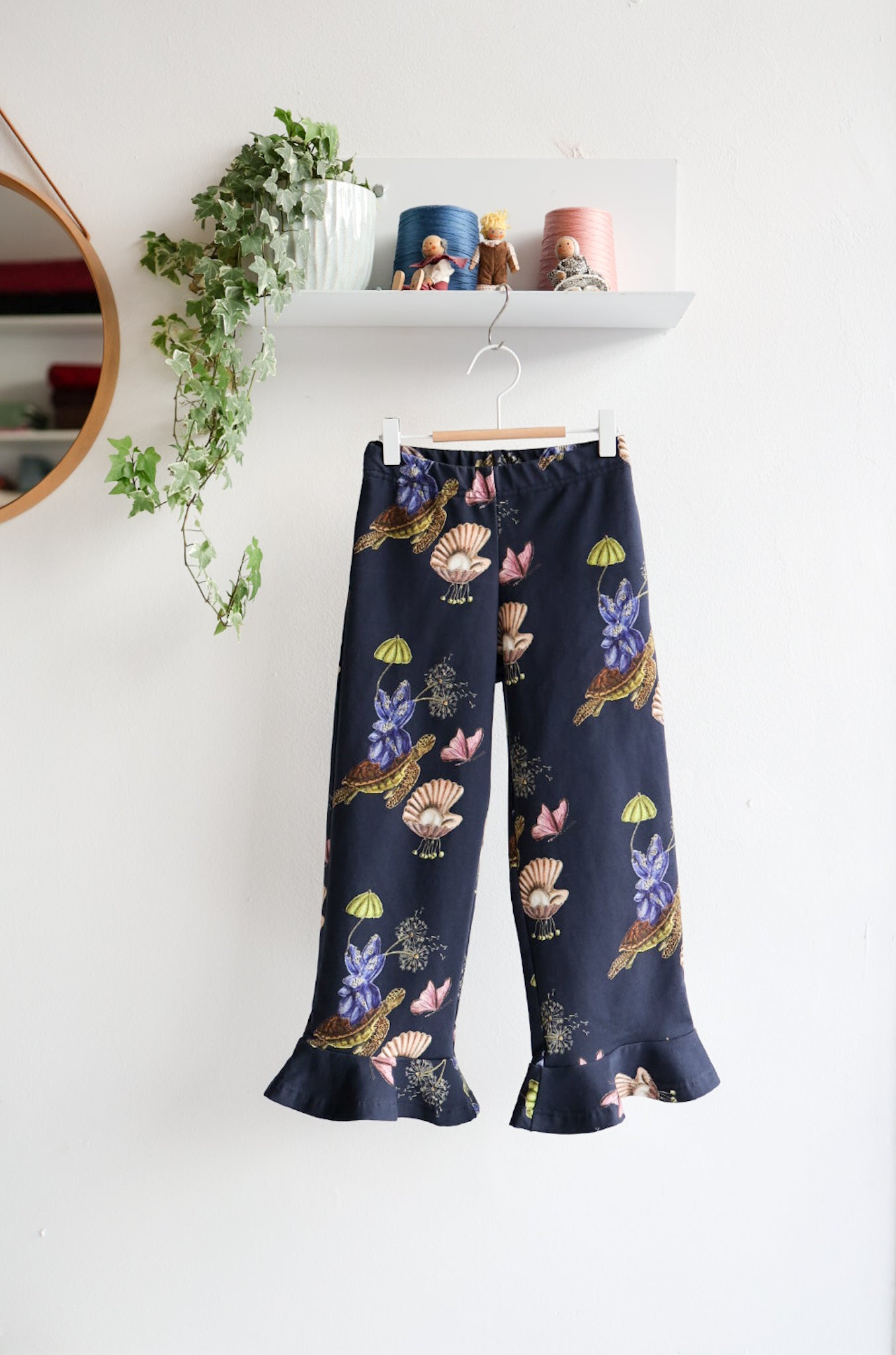Navy blue nature-patterned kids pants hanging against a white wall with decorative items.