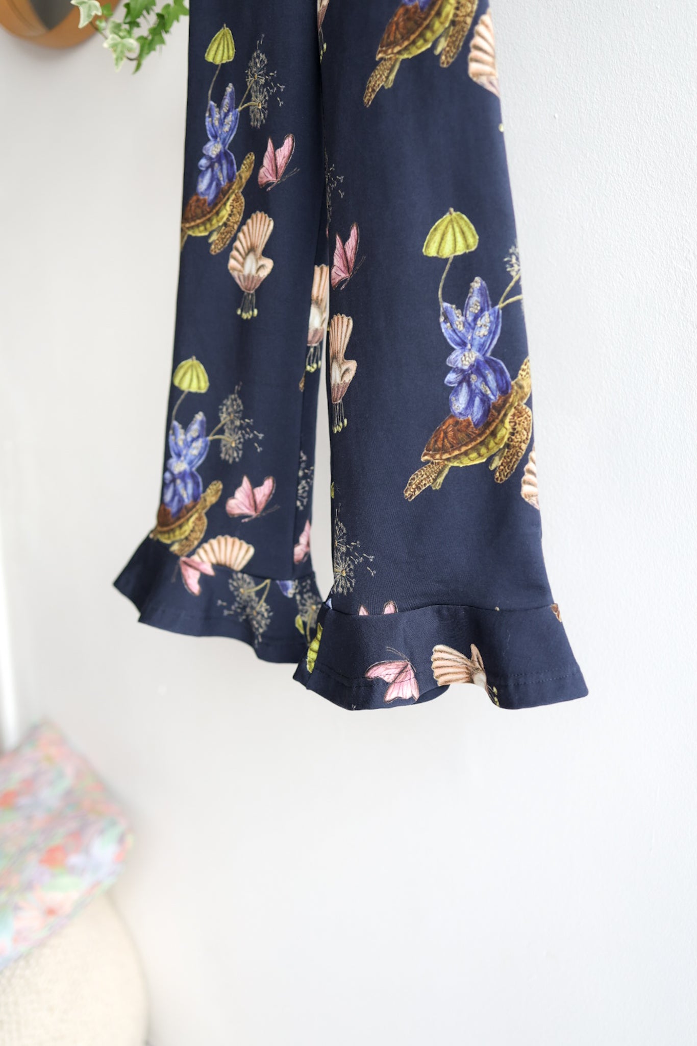 Navy blue nature-patterned kids pants hanging against a white wall.
