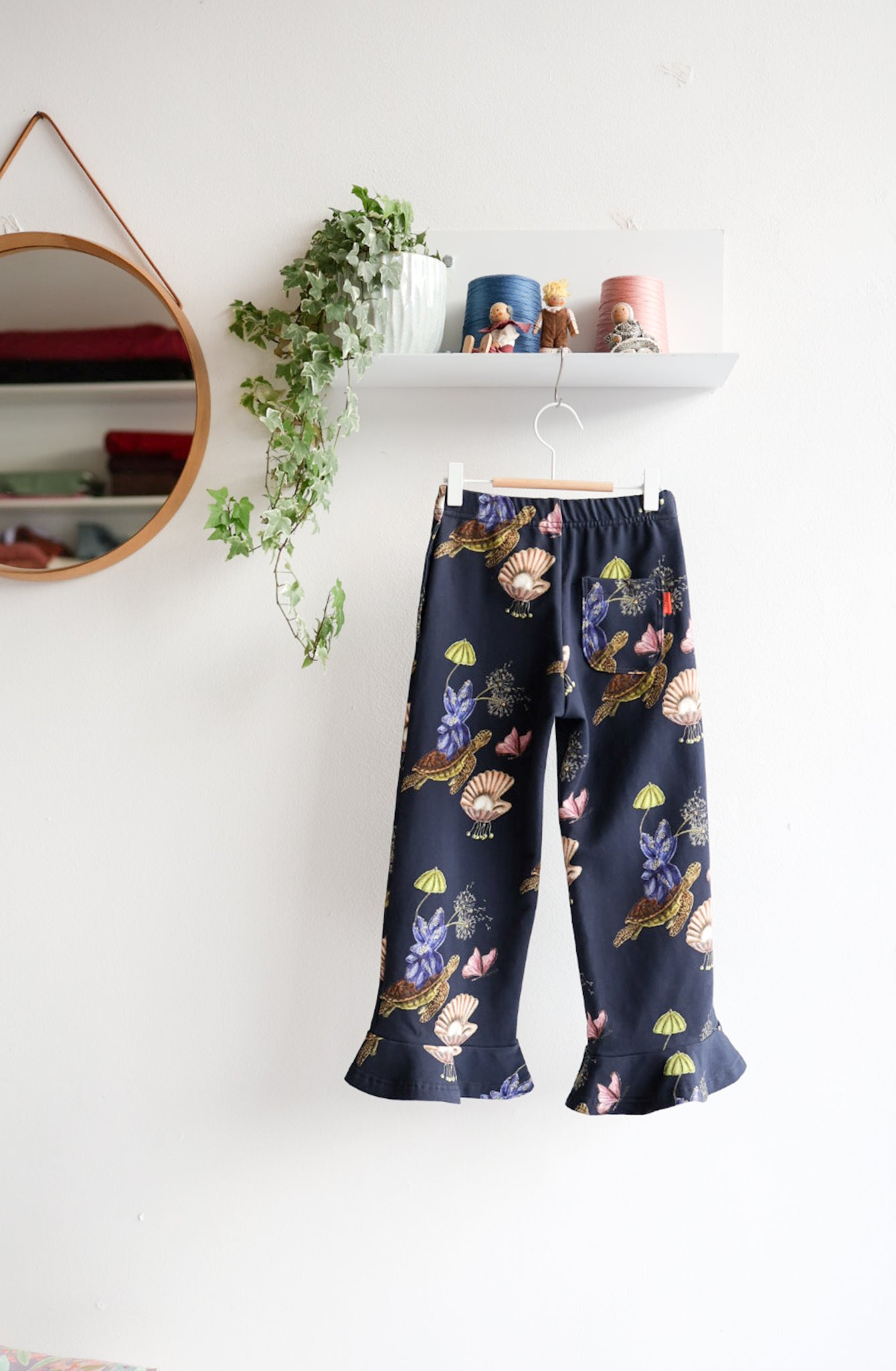 Navy blue nature-patterned kids pants hanging against a white wall with decorative items.