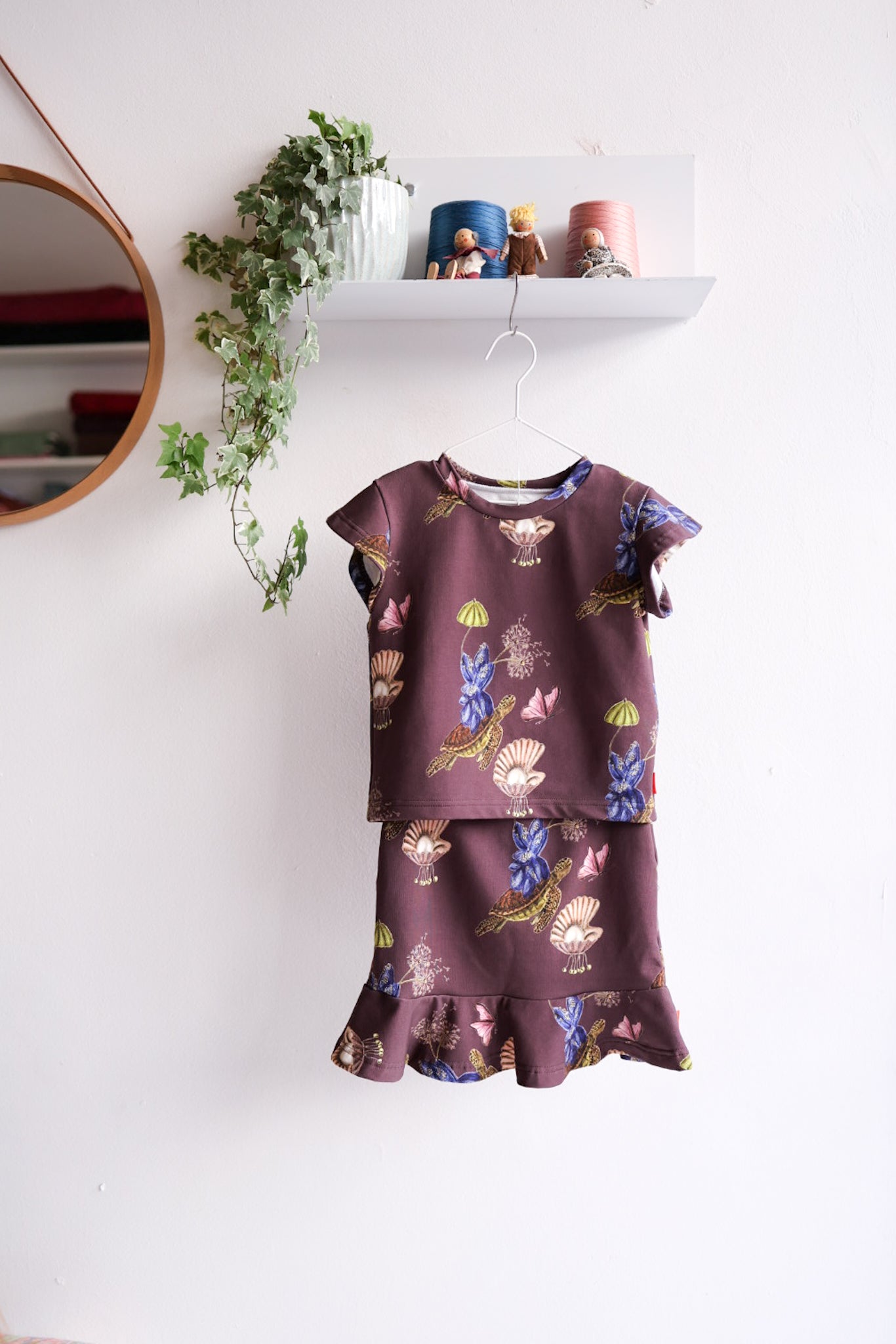 Kids skirt and top with floral pattern on a hanger against a white wall with decorative items.