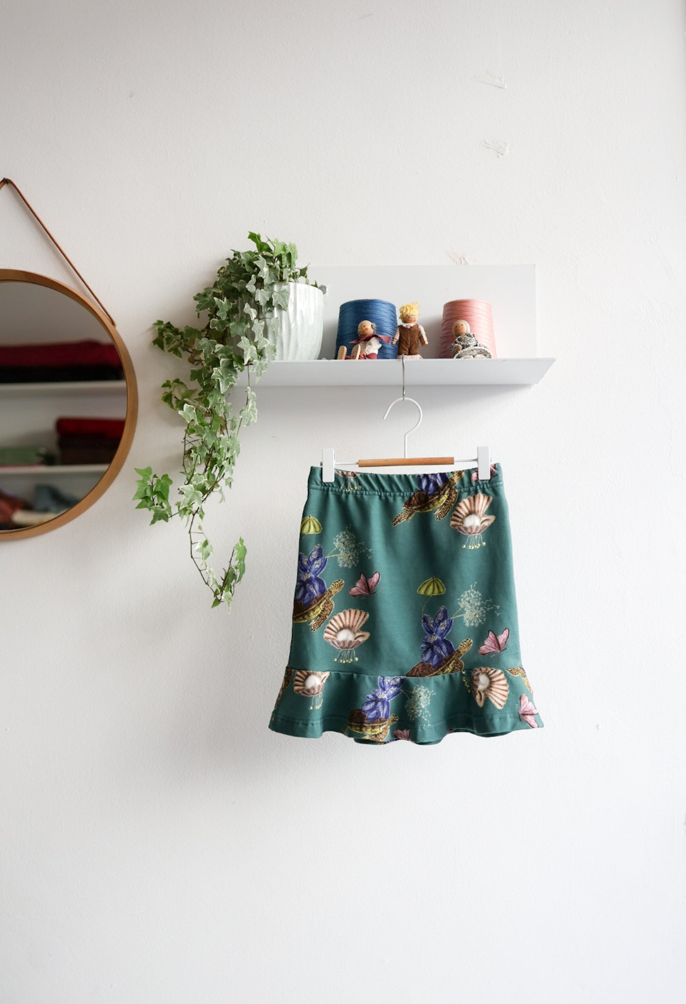 Teal kids skirt with nature-themed print hanging on a white wall.