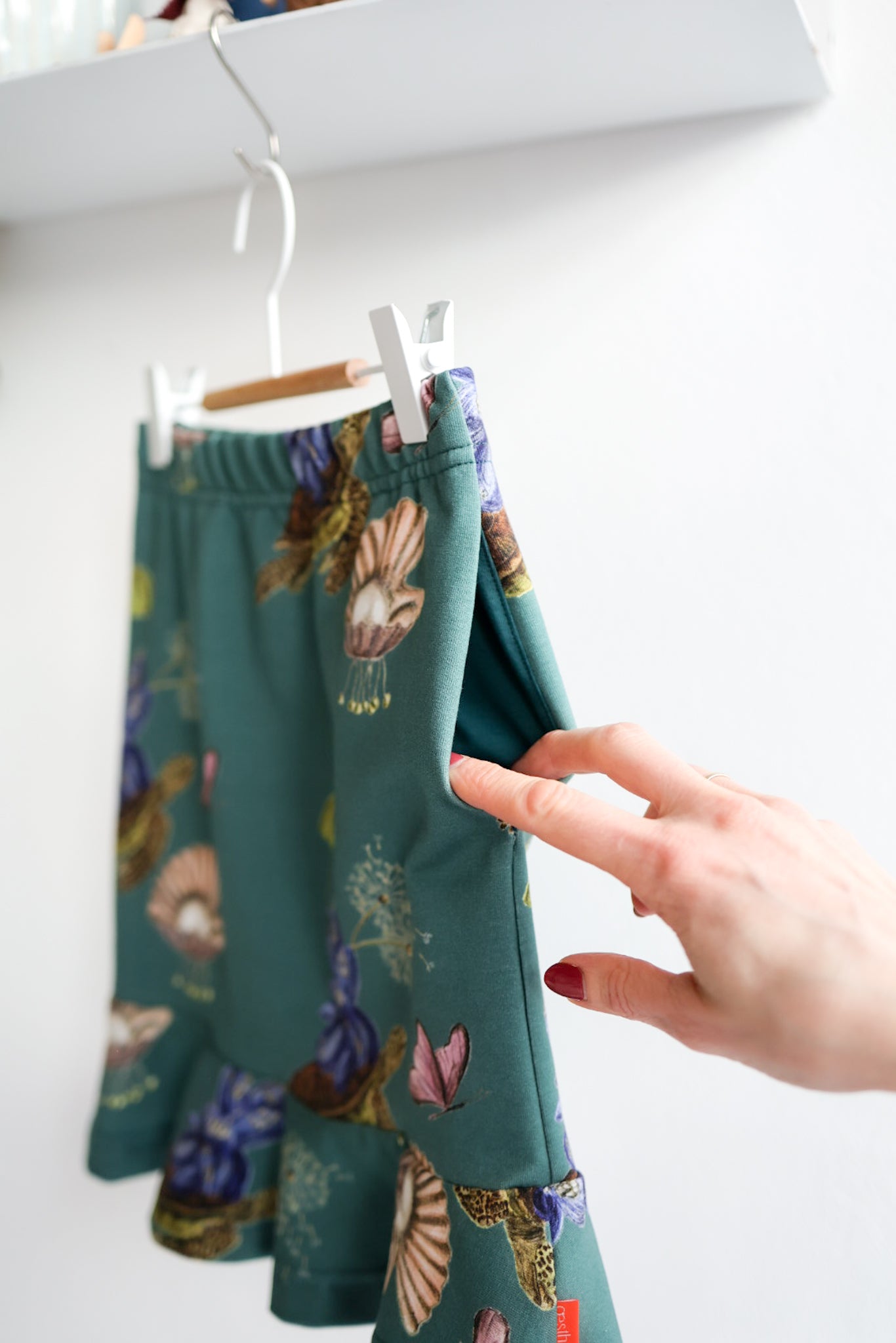 Teal kids skirt with nature-themed print hanging on a white wall.