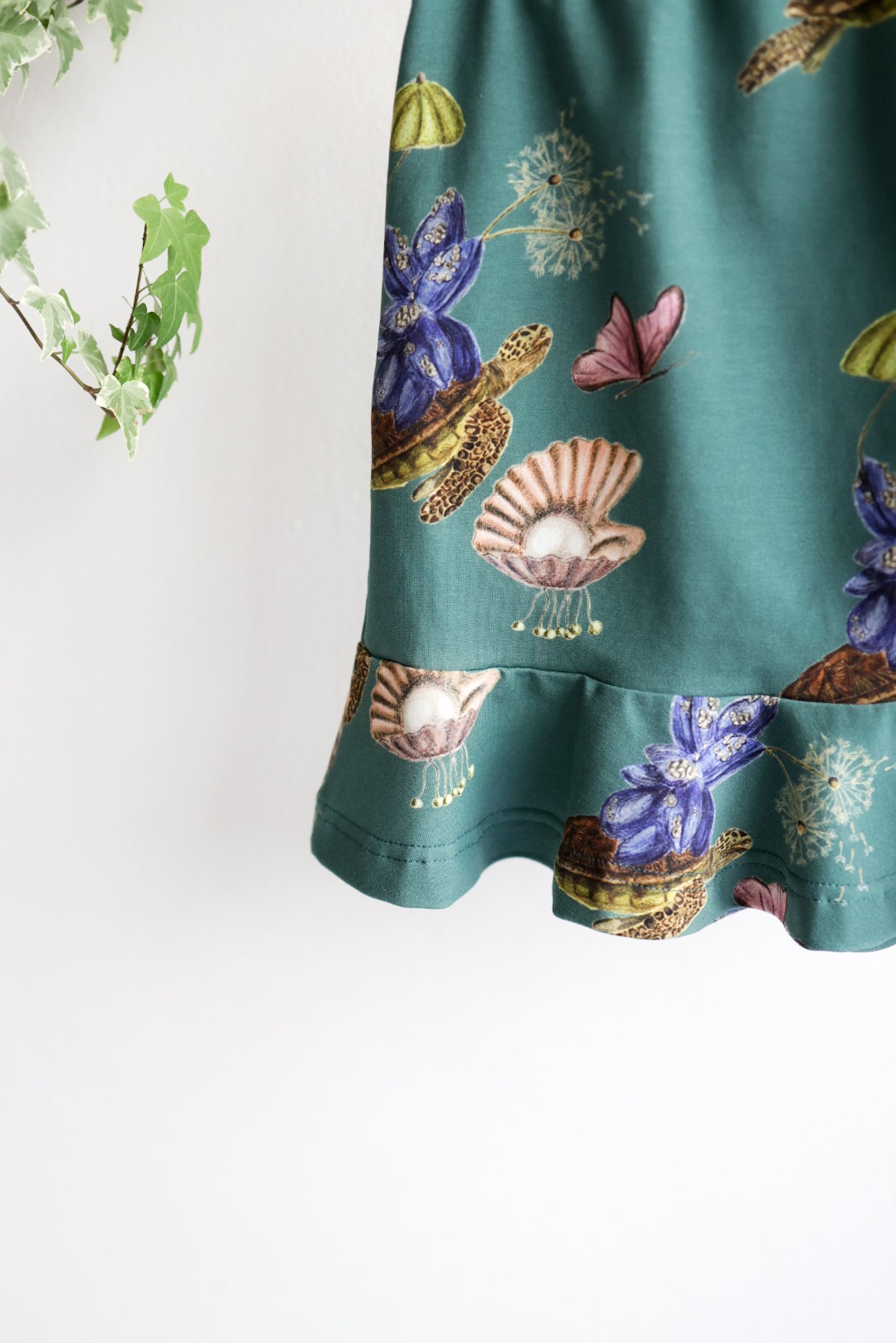 Teal kids skirt with nature-themed print featuring flowers, shells, and animals on a white background.
