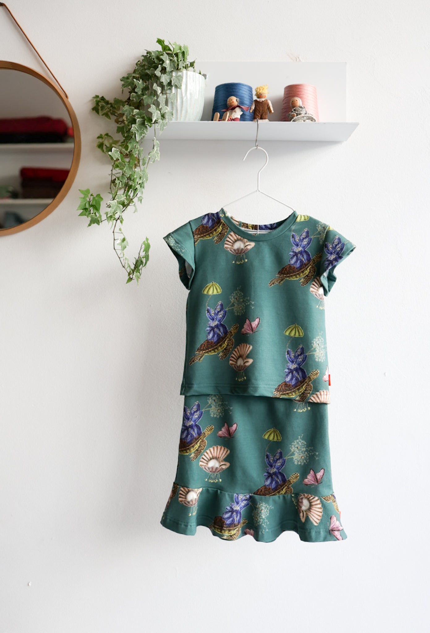 Teal kids skirt and top with nature-themed print hanging on a white background.