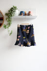 Navy blue kids skirt with colorful shell pattern hanging on a white wall.
