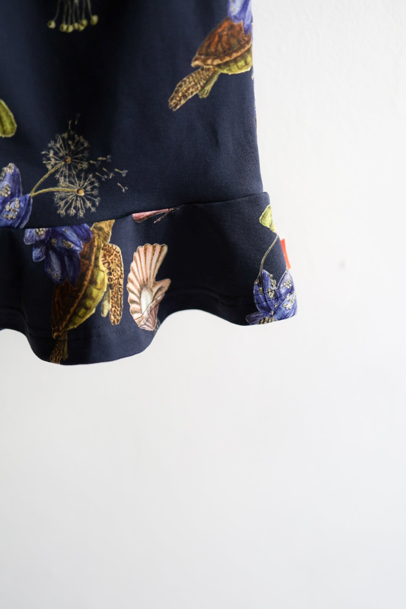 Navy blue kids skirt with colorful shell pattern hanging on a white wall.