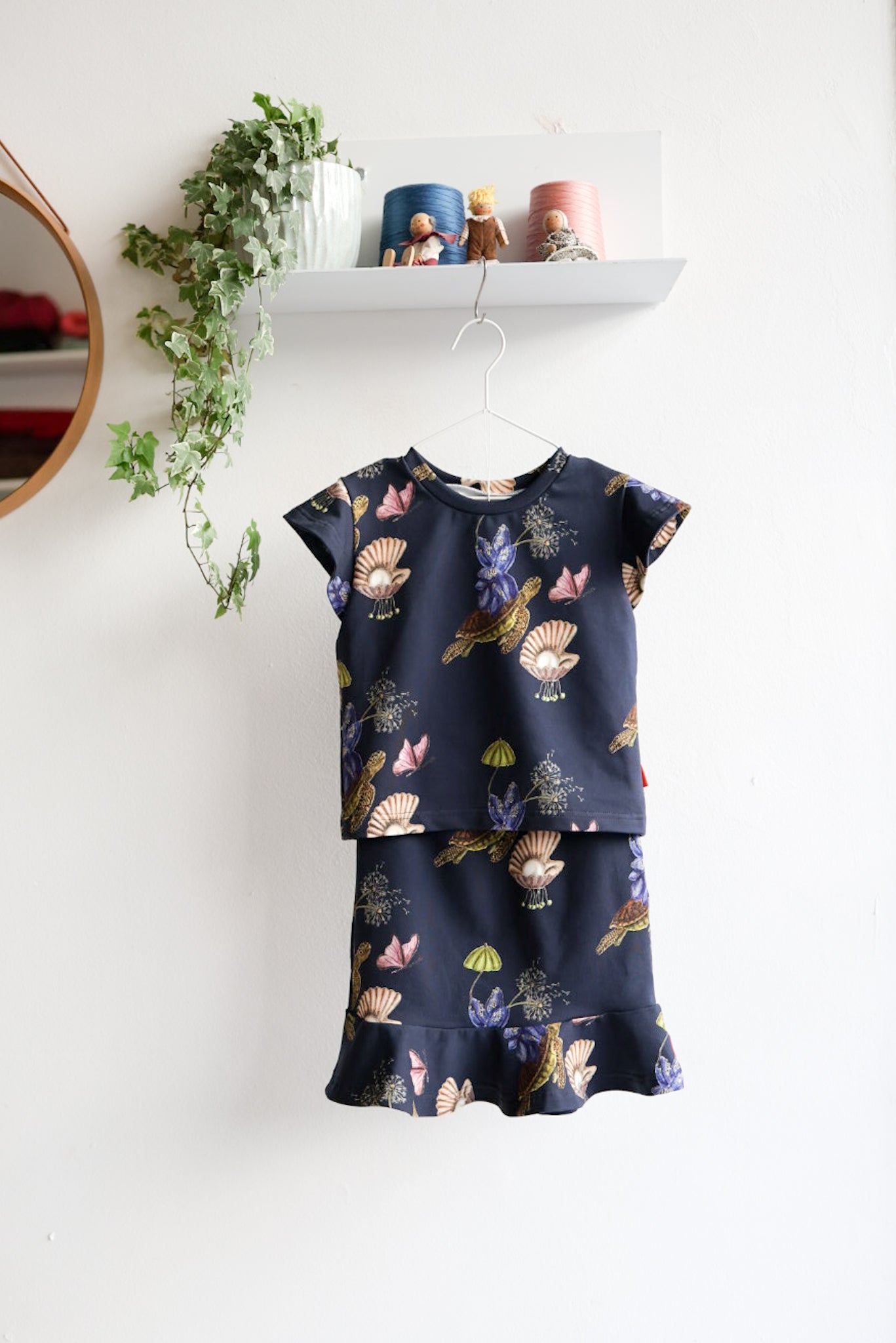 Navy blue kids skirt and top with colorful shell pattern hanging on a white wall.