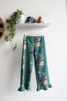 Teal nature-patterned kids pants hanging against a white wall with decorative items.