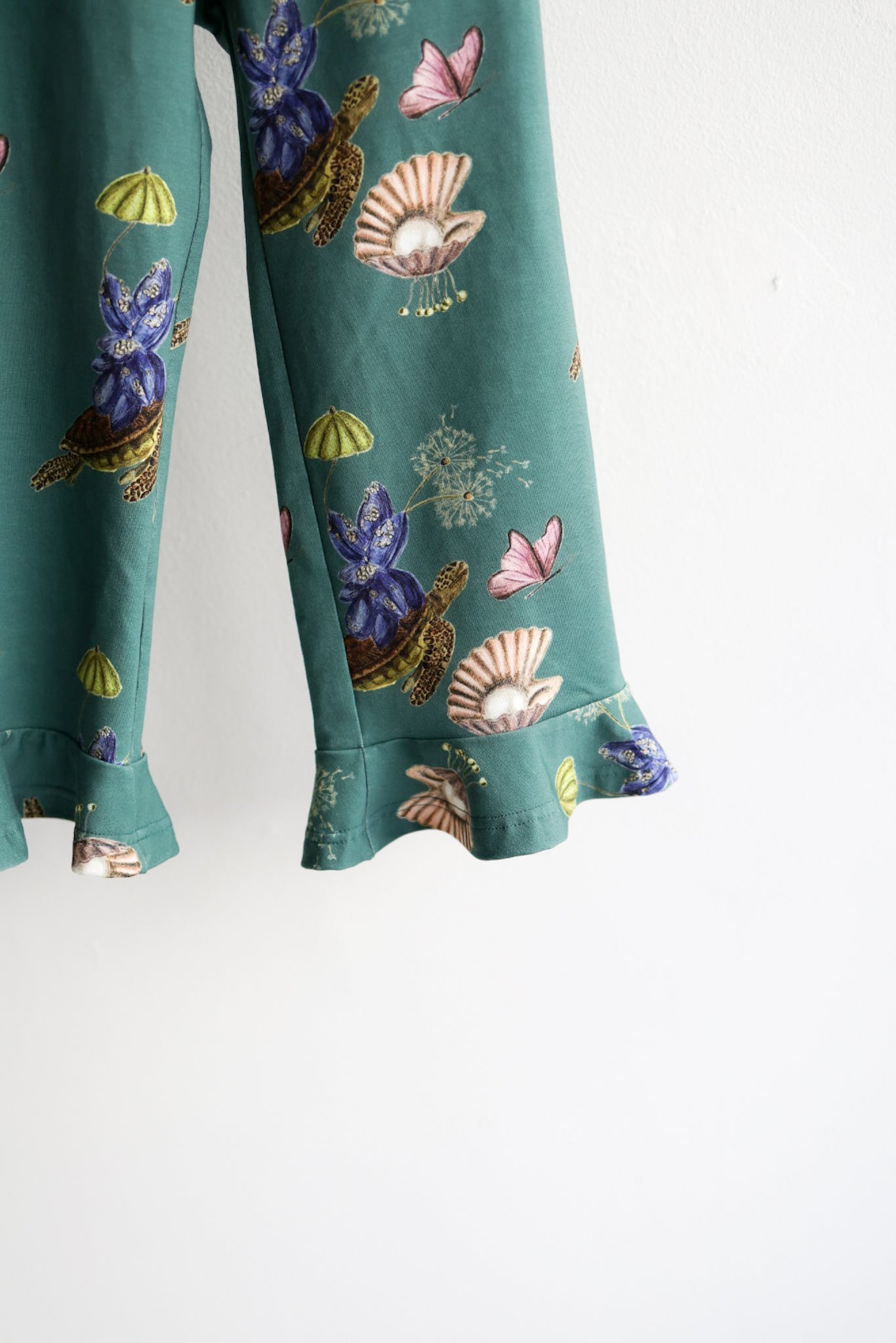 Teal nature-patterned kids pants hanging against a white wall.