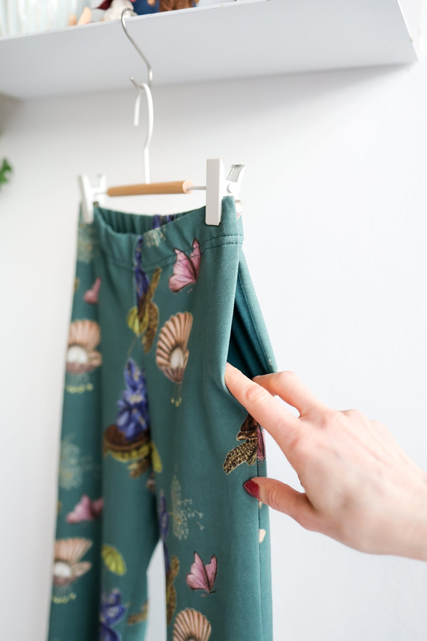 Teal nature-patterned kids pants hanging against a white wall.