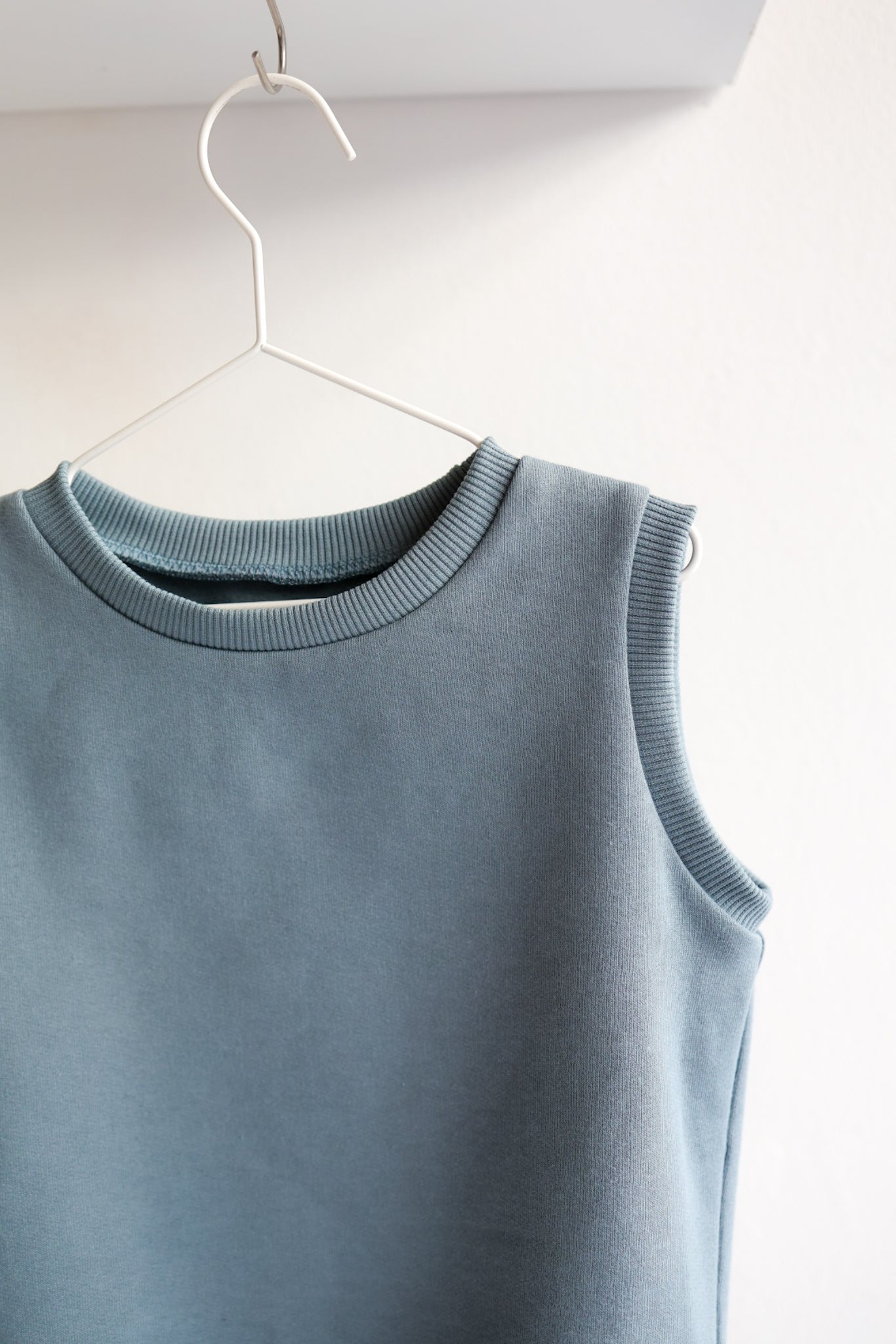 Blue kids sleeveless top on a hanger against a white background.
