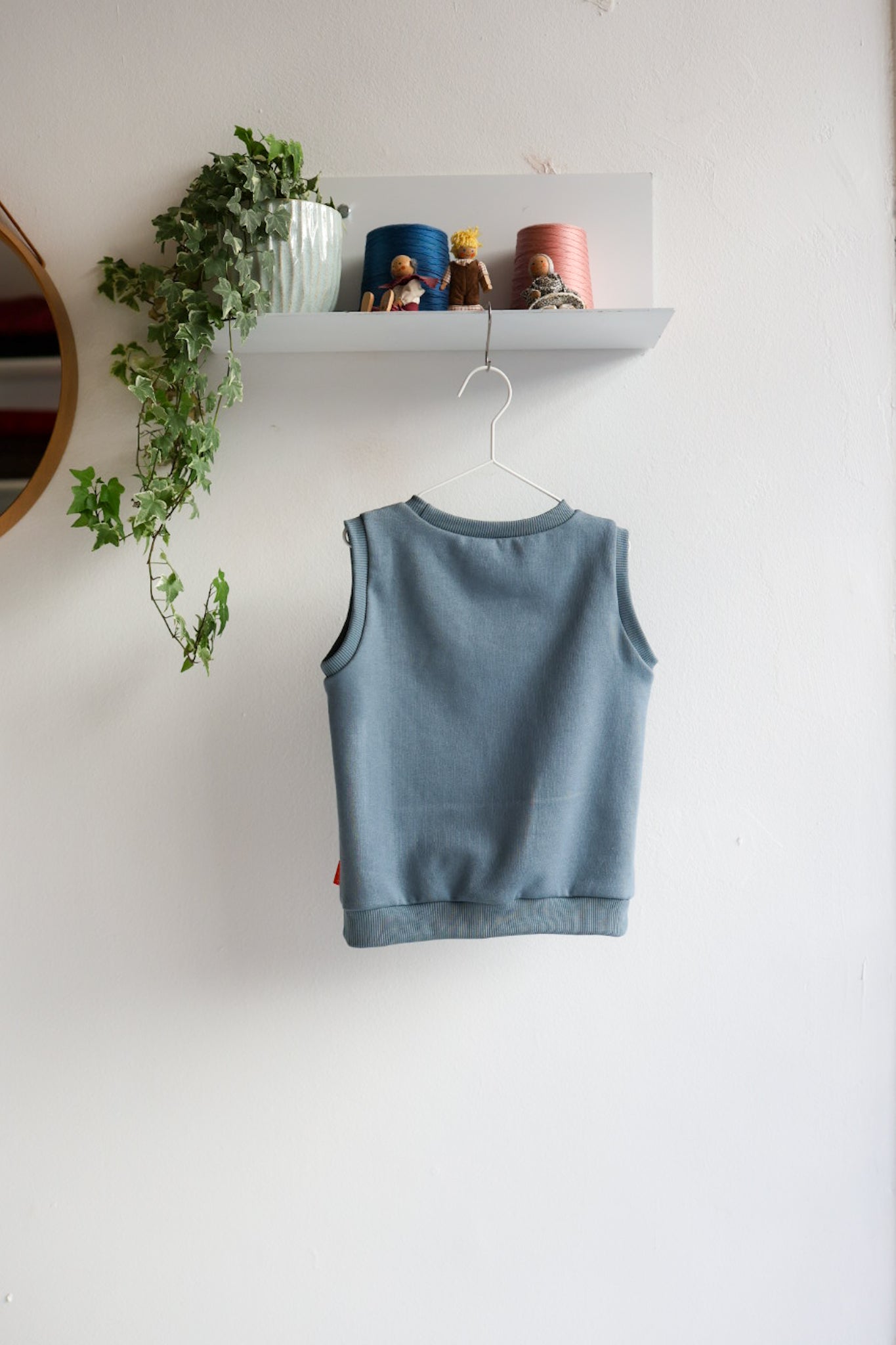 Blue kids sleeveless top hanging on a white wall with decorative items above.