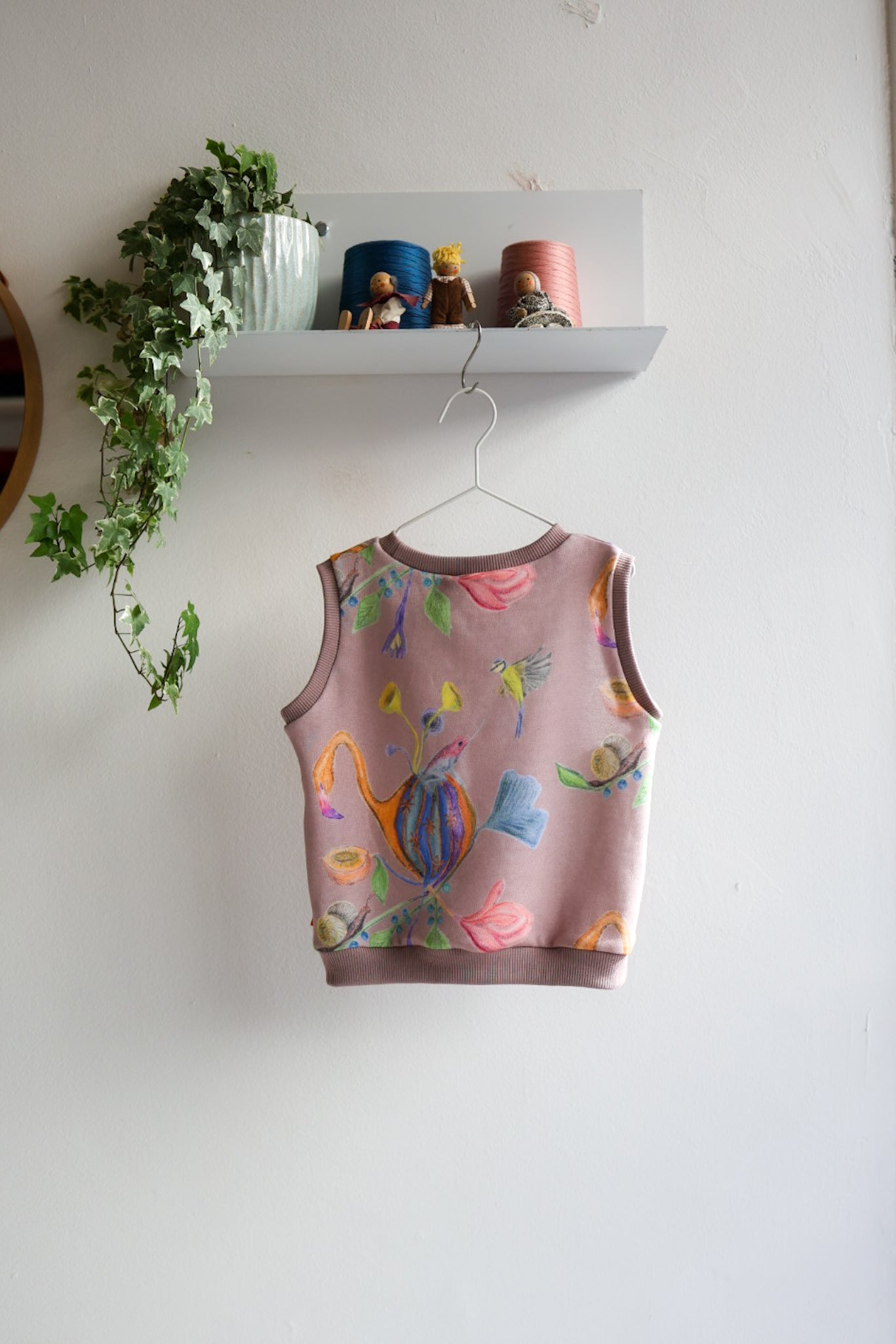 Kids sleeveless top with colorful designs on a hanger against a white wall.