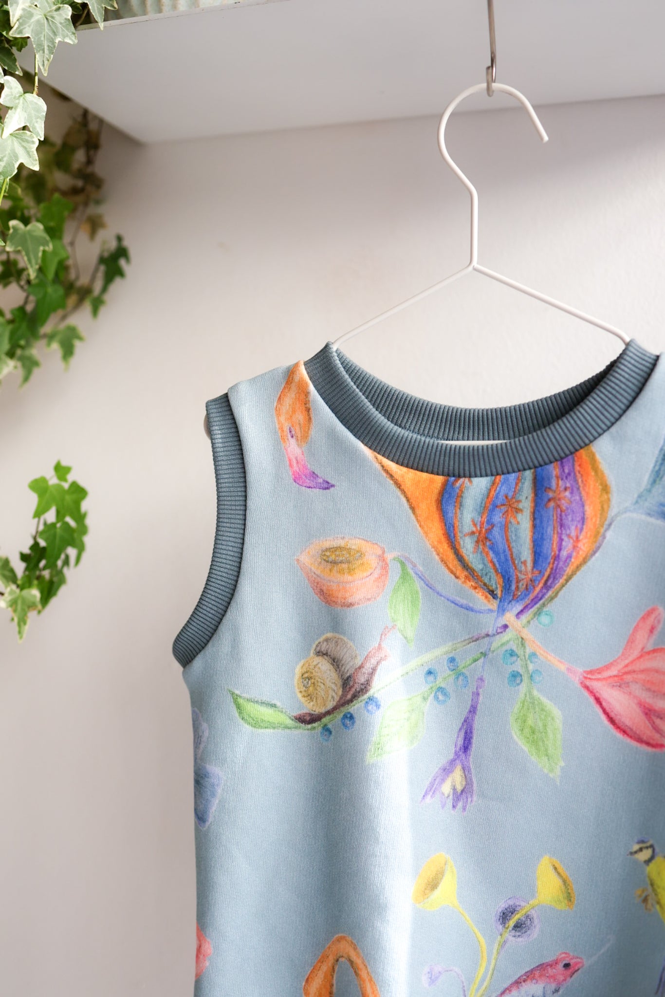 Colorful kids sleeveless top with floral design on a hanger against a light background.