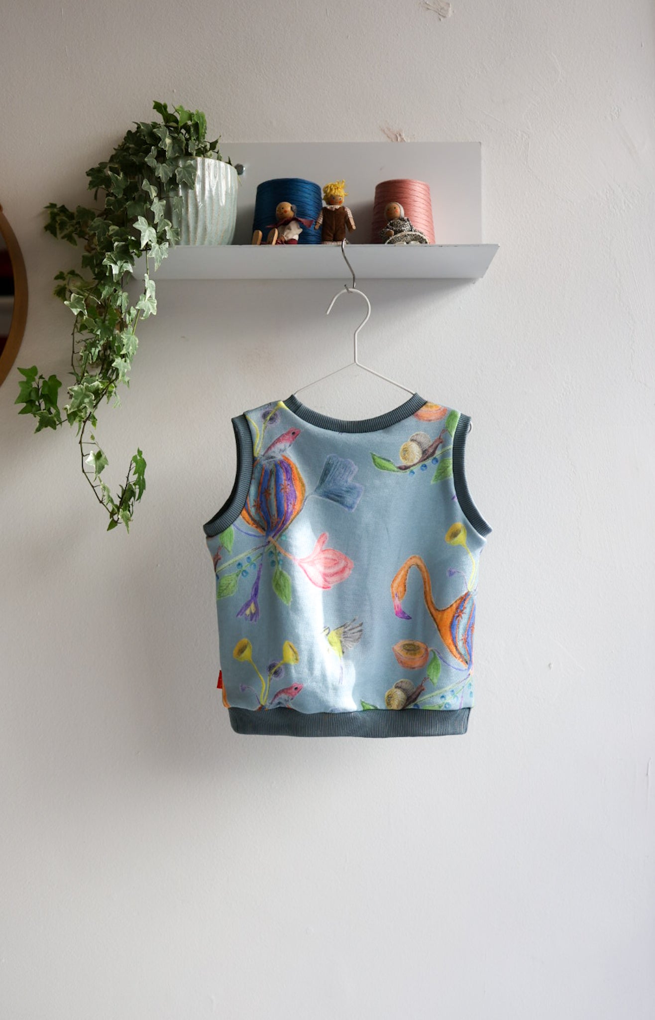 Children's sleeveless shirt with floral pattern on a hanger against a white wall.