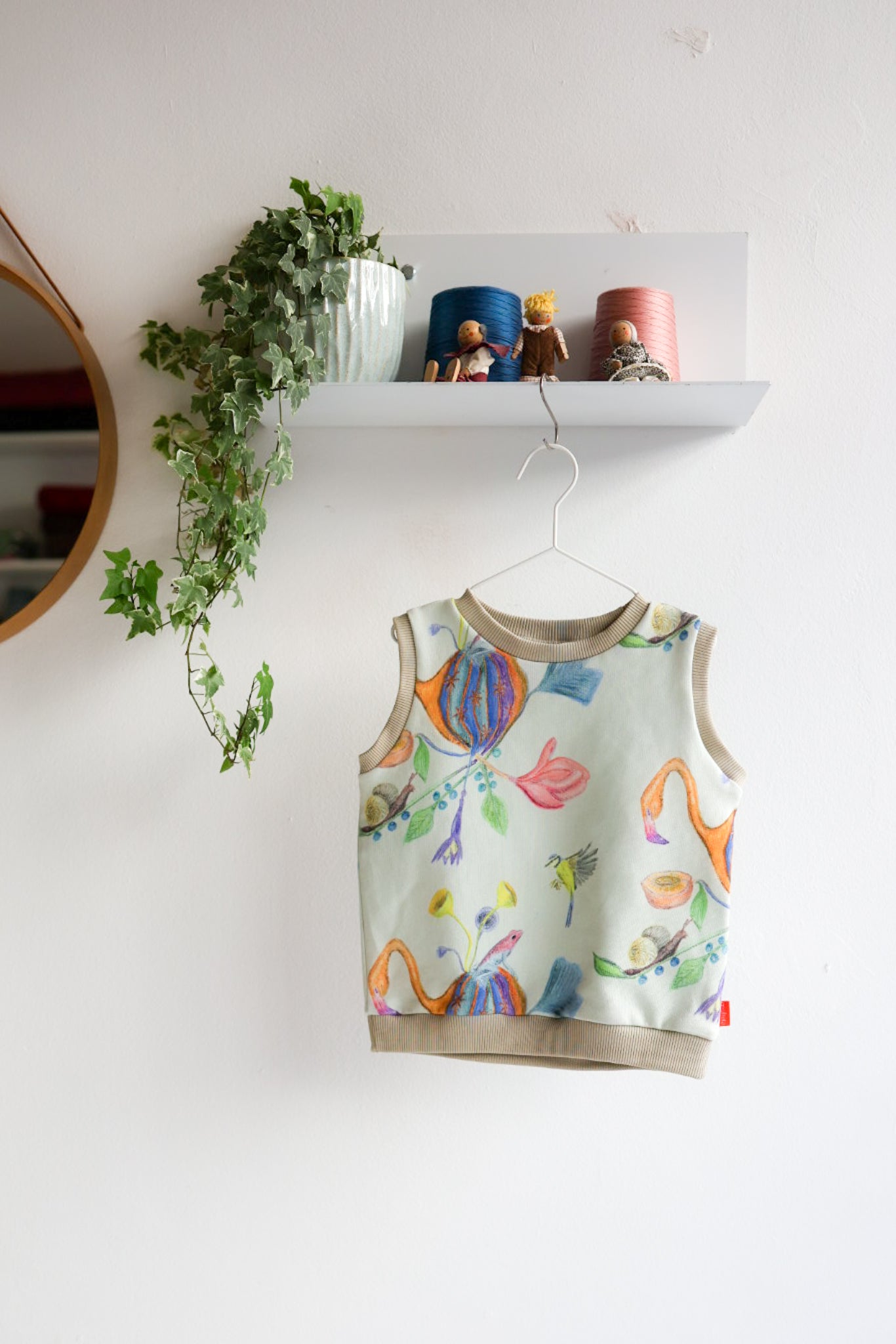 Colorful kids sleeveless top with floral designs hanging on a white wall.