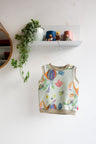 Colorful kids sleeveless top with floral designs hanging on a white wall.