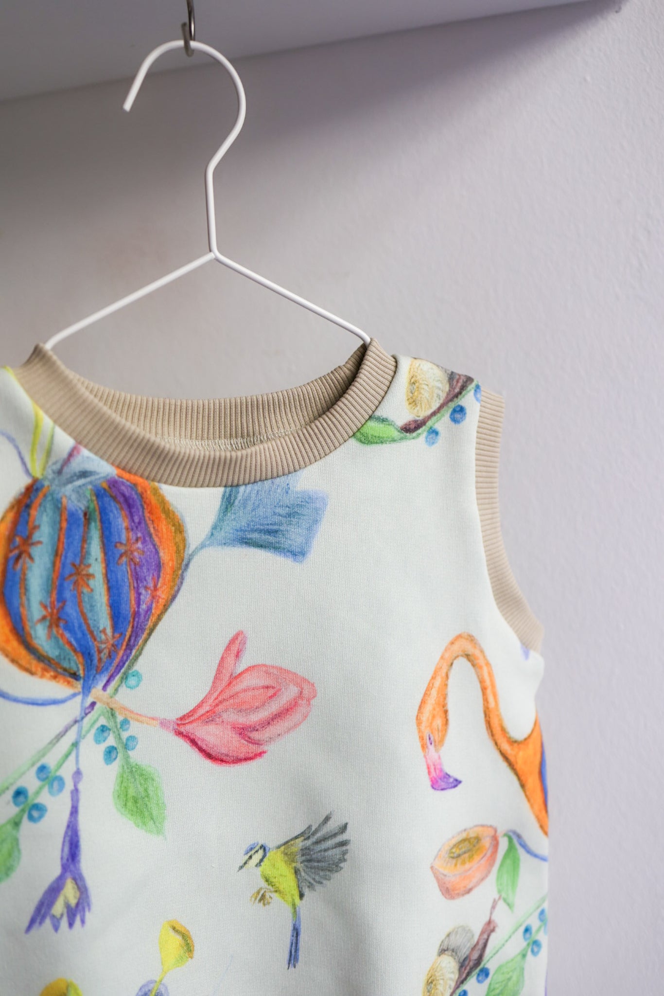 Colorful kids sleeveless top with floral designs on a hanger against a plain background