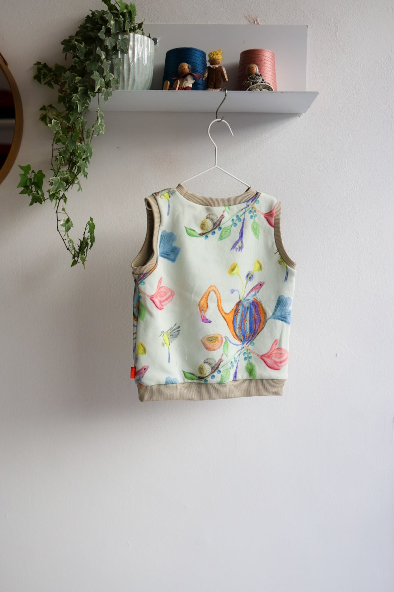 Colorful kids sleeveless top with floral design hanging on a white wall.