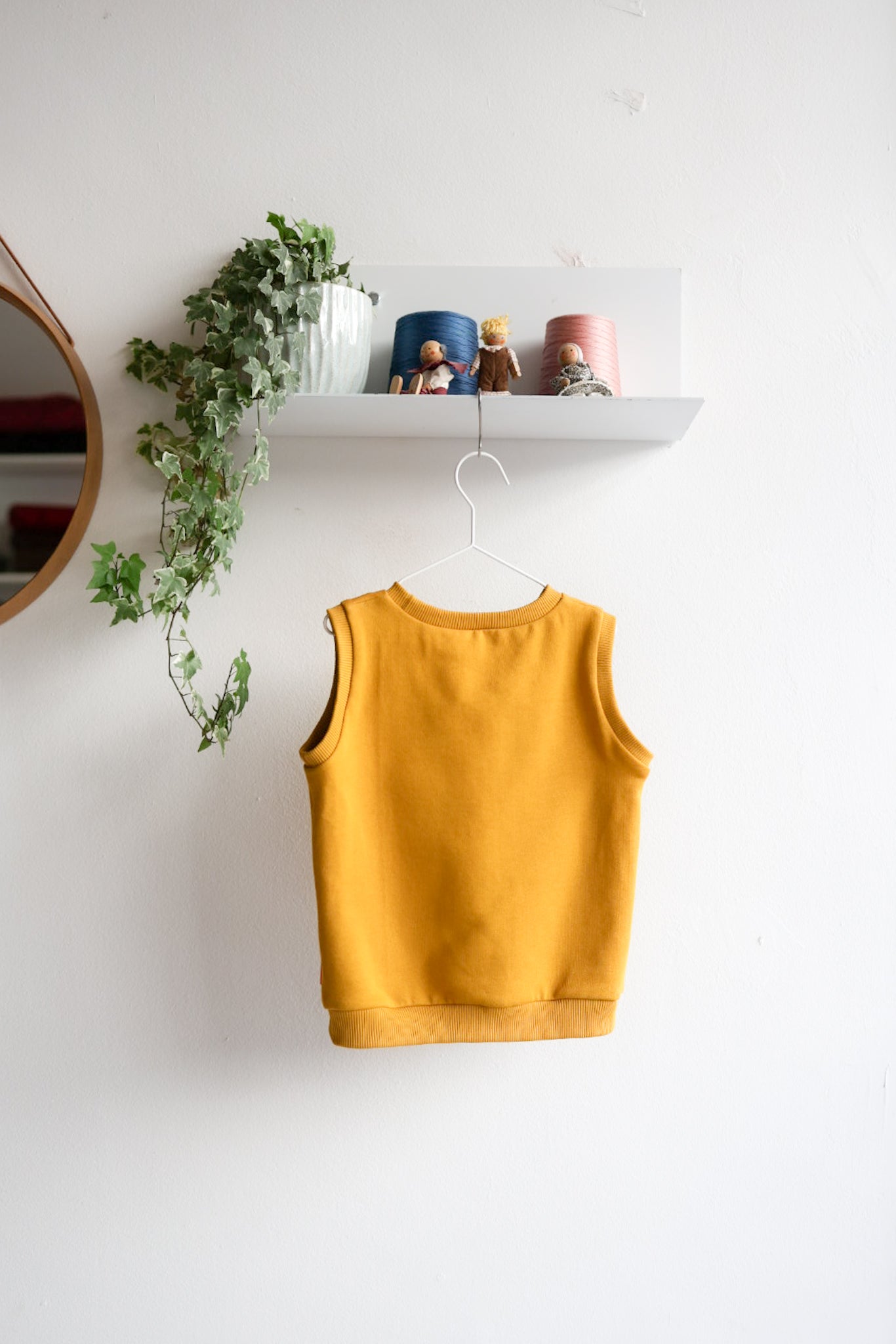 Yellow kids sleeveless top hanging on a white wall with decorative items above.