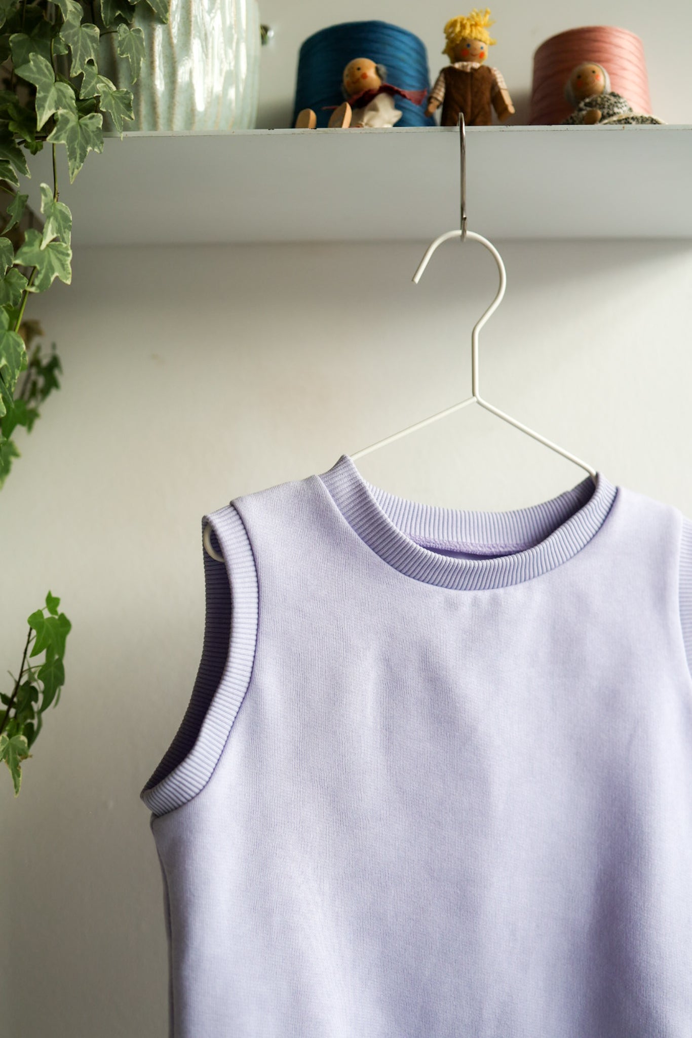 Lavender kids sleeveless top on a hanger with a shelf in the background.