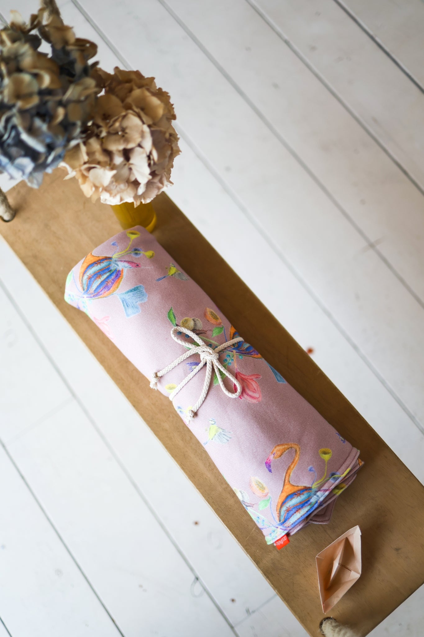 Rolled-up colorful babies blanket with a bow on a white wooden floor